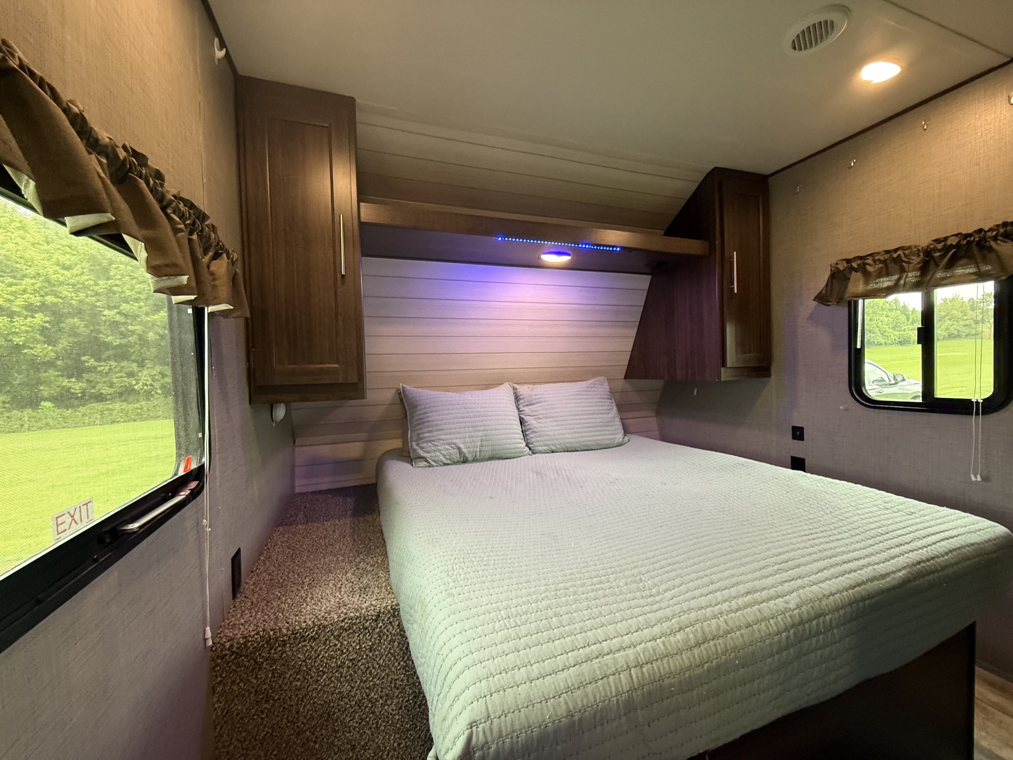 Comfortable RV rental bedroom featuring a soft bed, ambient lighting, overhead storage, and windows with outdoor views.. Crossroads RV Zinger 2019