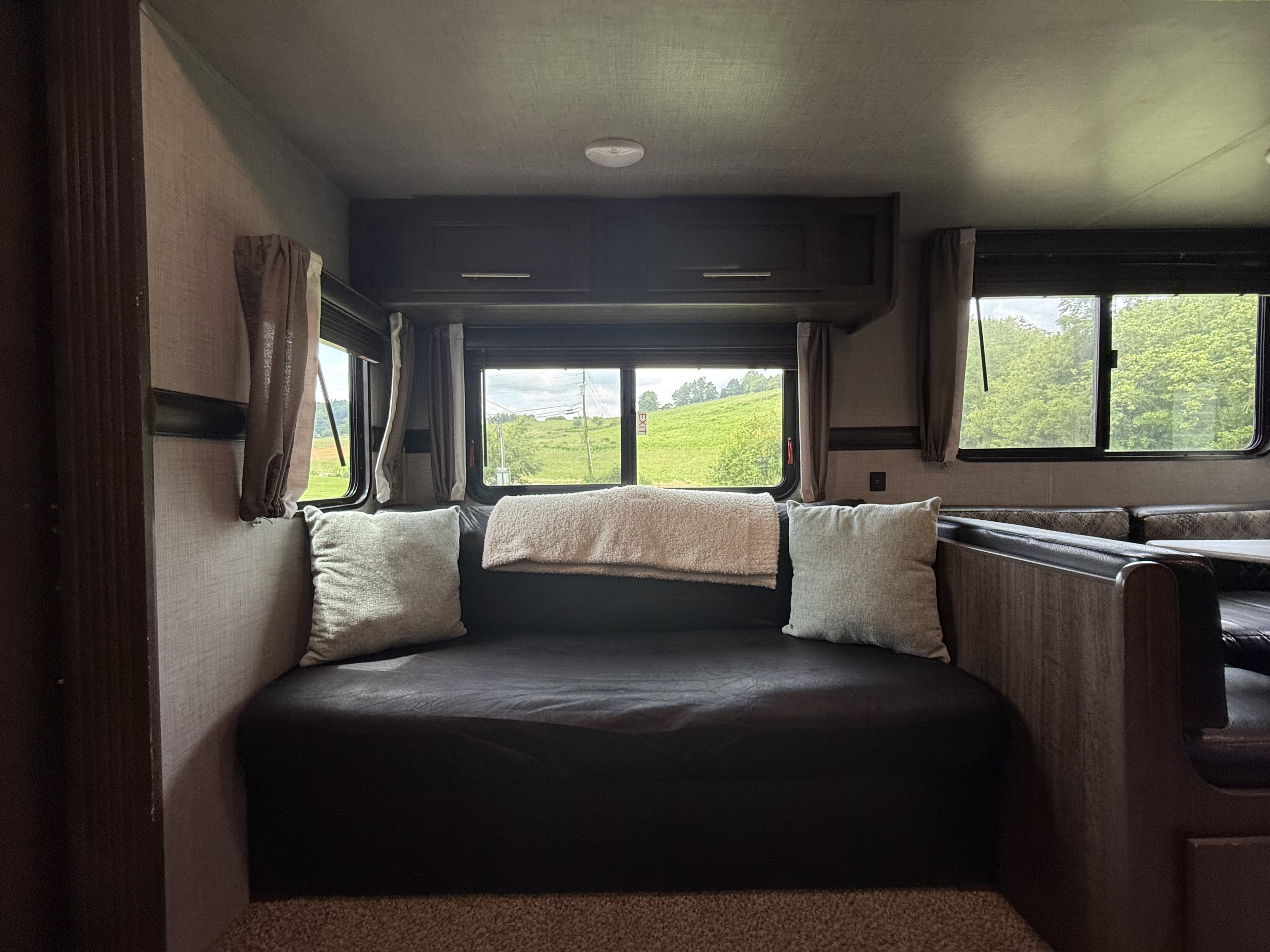 Cozy RV rental interior with a bed/sofa, windows overlooking green hills, and a dining area. Ideal camper living space.. Crossroads RV Zinger 2019