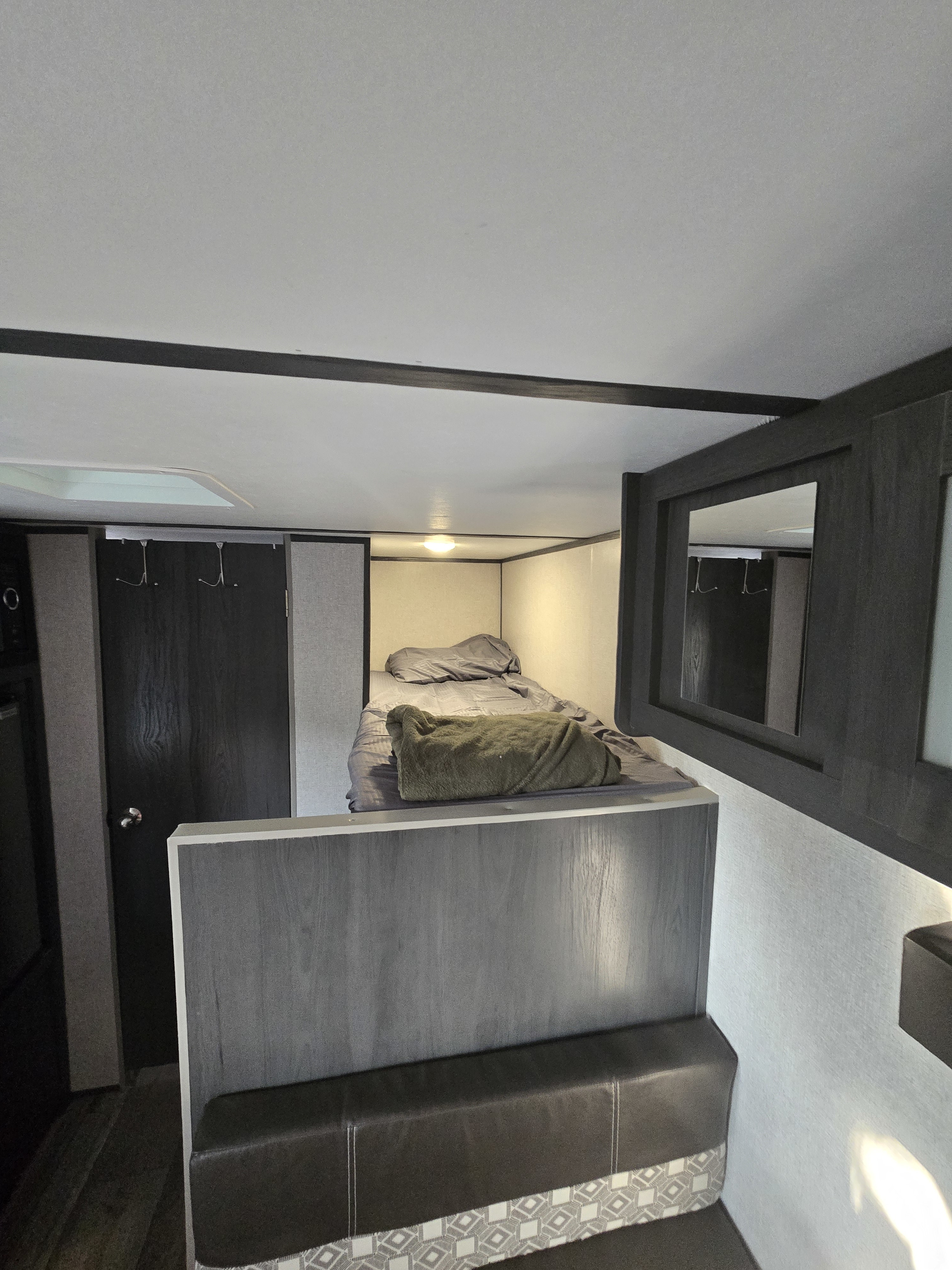 Cozy RV rental interior with a neatly made bunk bed, modern dark and light grey finishes, and a small mirror.. Dutchmen ASPEN TRAIL 17BH 2021