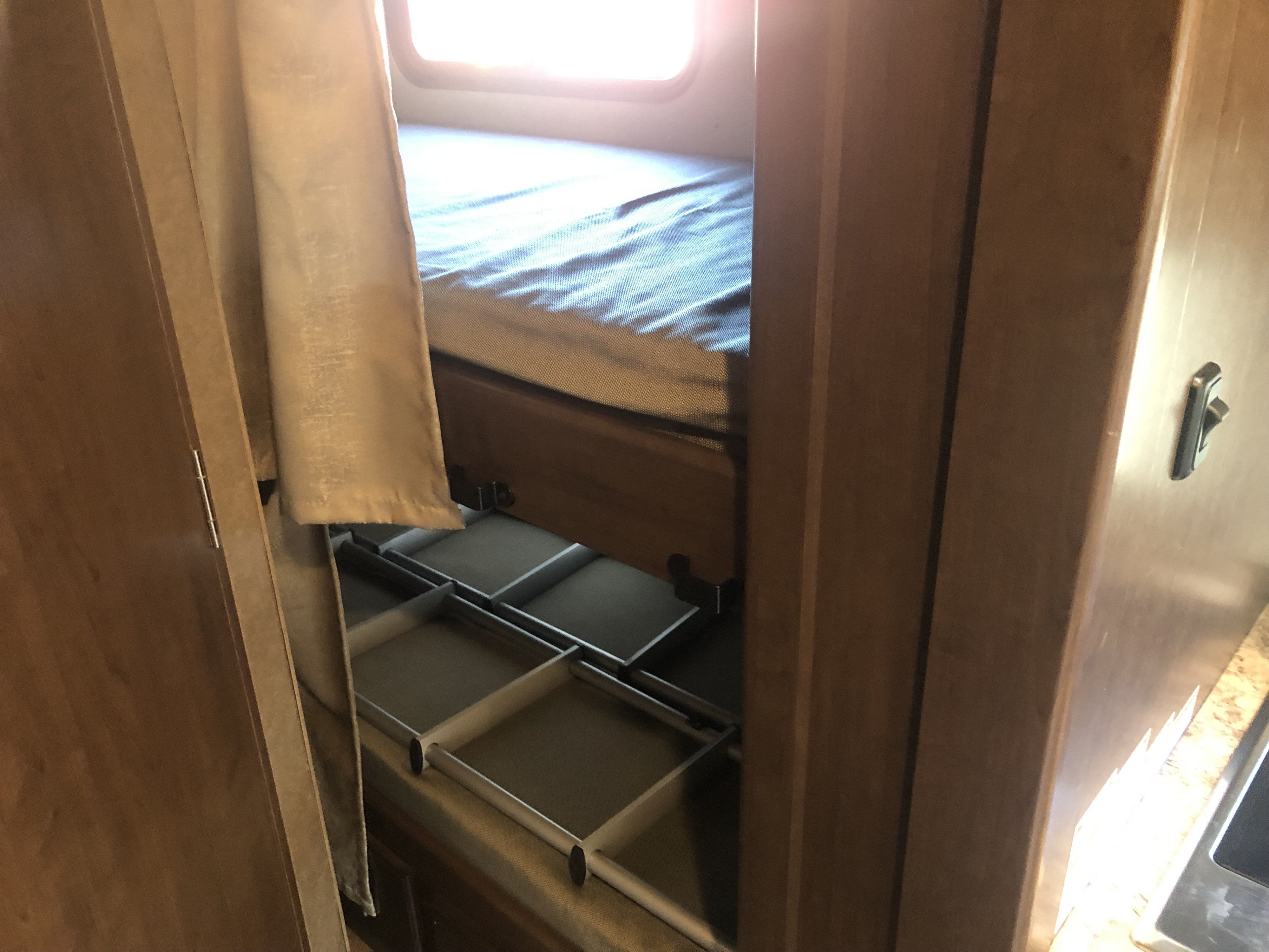 Inside an RV rental: a comfortable bunk bed with a bright window, and practical pull-out storage bins below.. Thor Chateau 2020