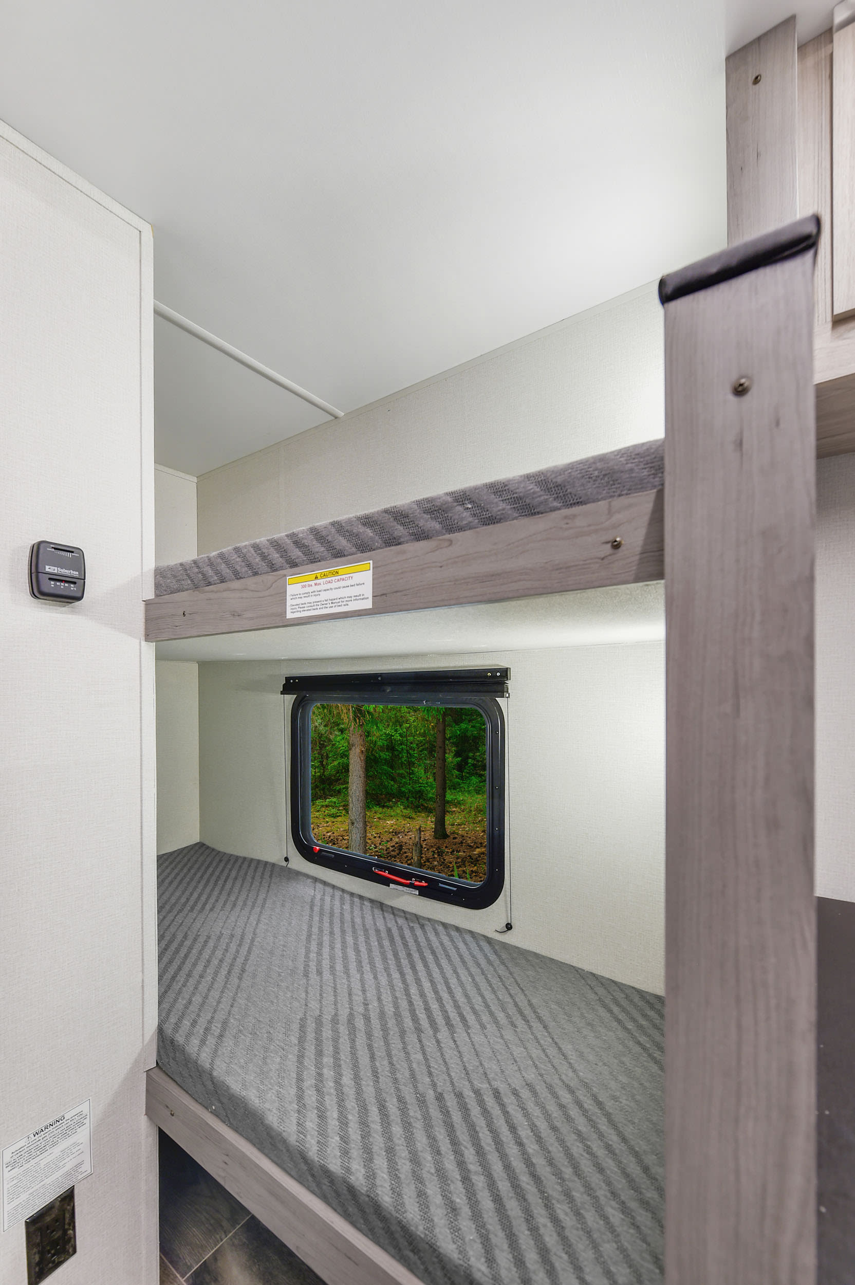 Cozy RV rental interior featuring comfortable bunk beds with a window view of a serene forest. Perfect for travel!. Heartland RVs Mallard 2025