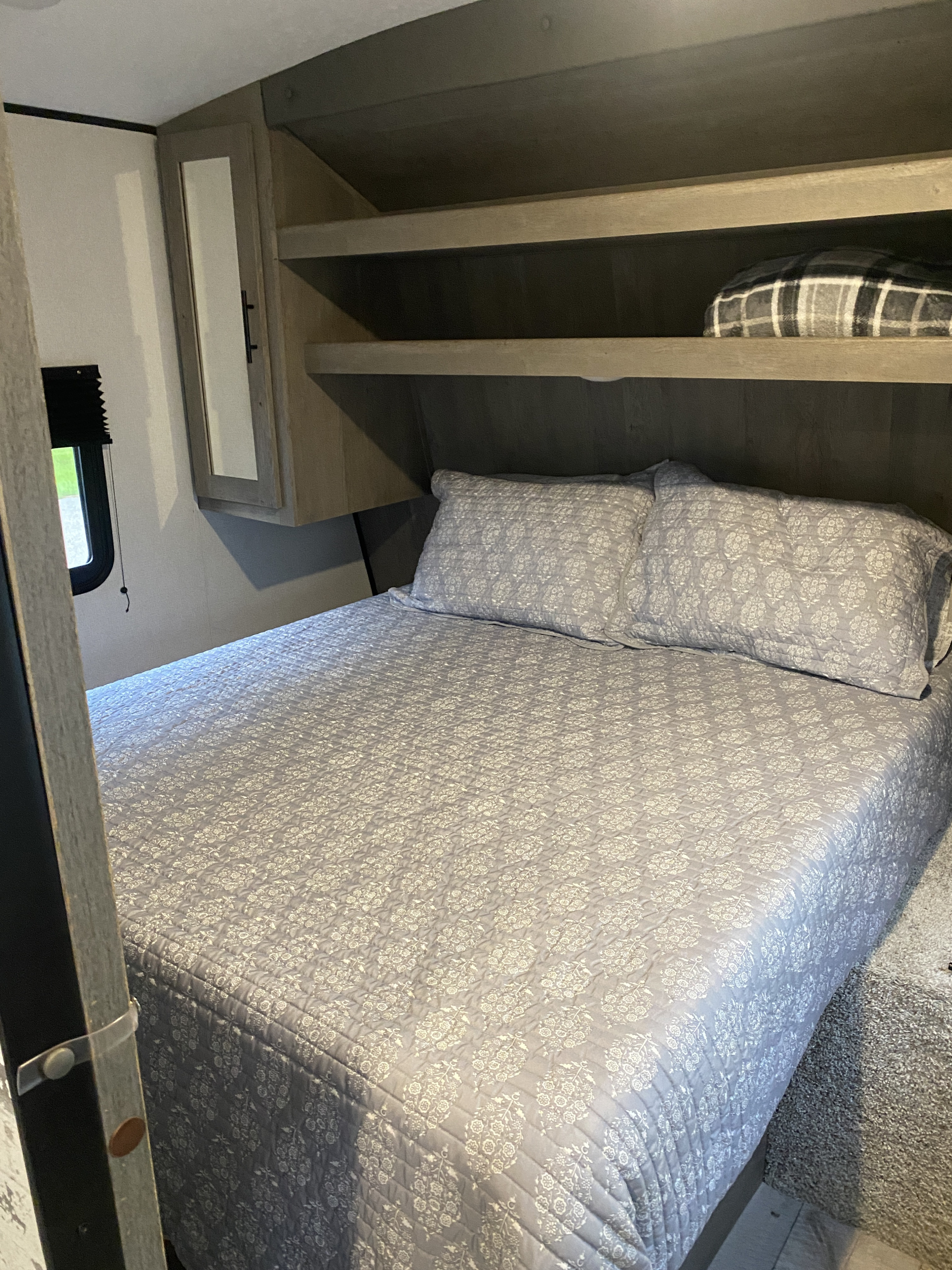 Inside an RV rental: a cozy bedroom featuring a patterned bed, pillows, and functional built-in shelves.. Keystone RV Springdale 2021