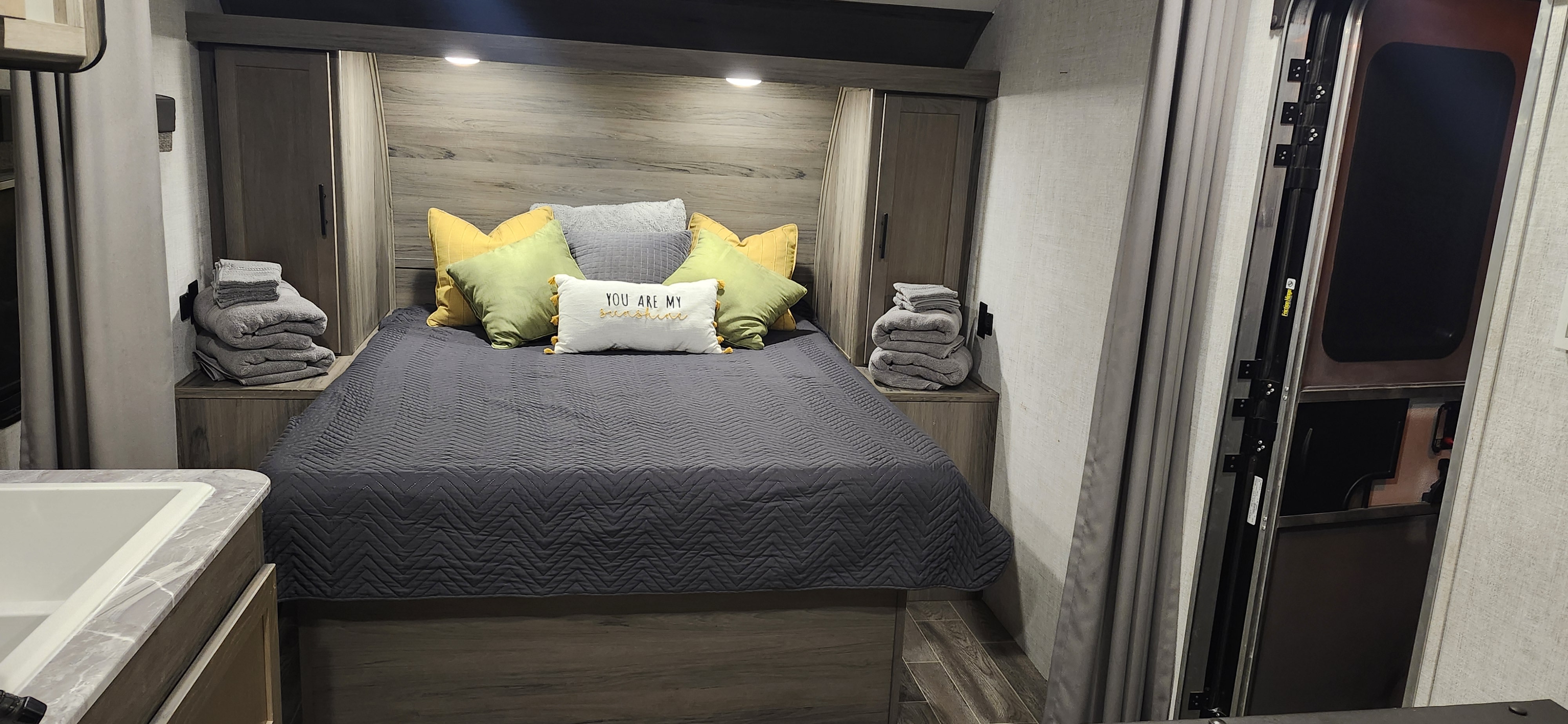Inside a cozy RV rental, this bedroom boasts a comfortable bed with cheerful pillows, built-in storage, and fresh towels ready.. Gulf Stream Enlighten 2021