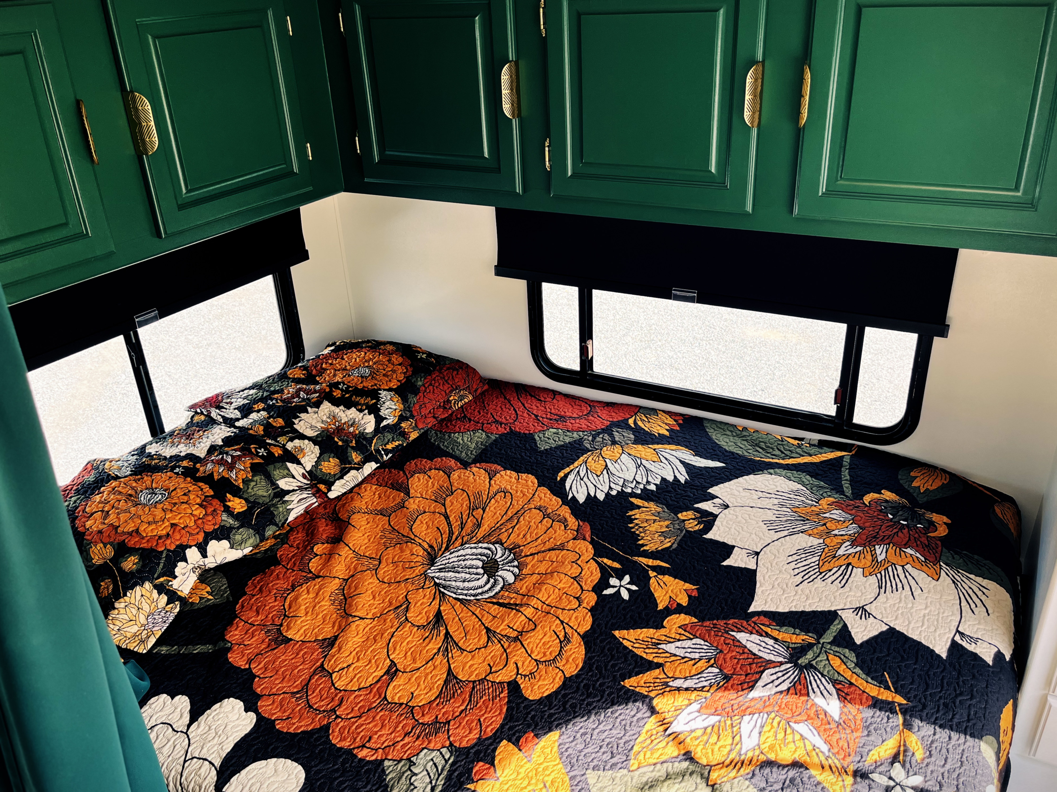 Cozy RV rental bedroom features emerald cabinets & a bed with a vibrant floral quilt, flanked by windows.. Coachmen Freelander Premier 2006