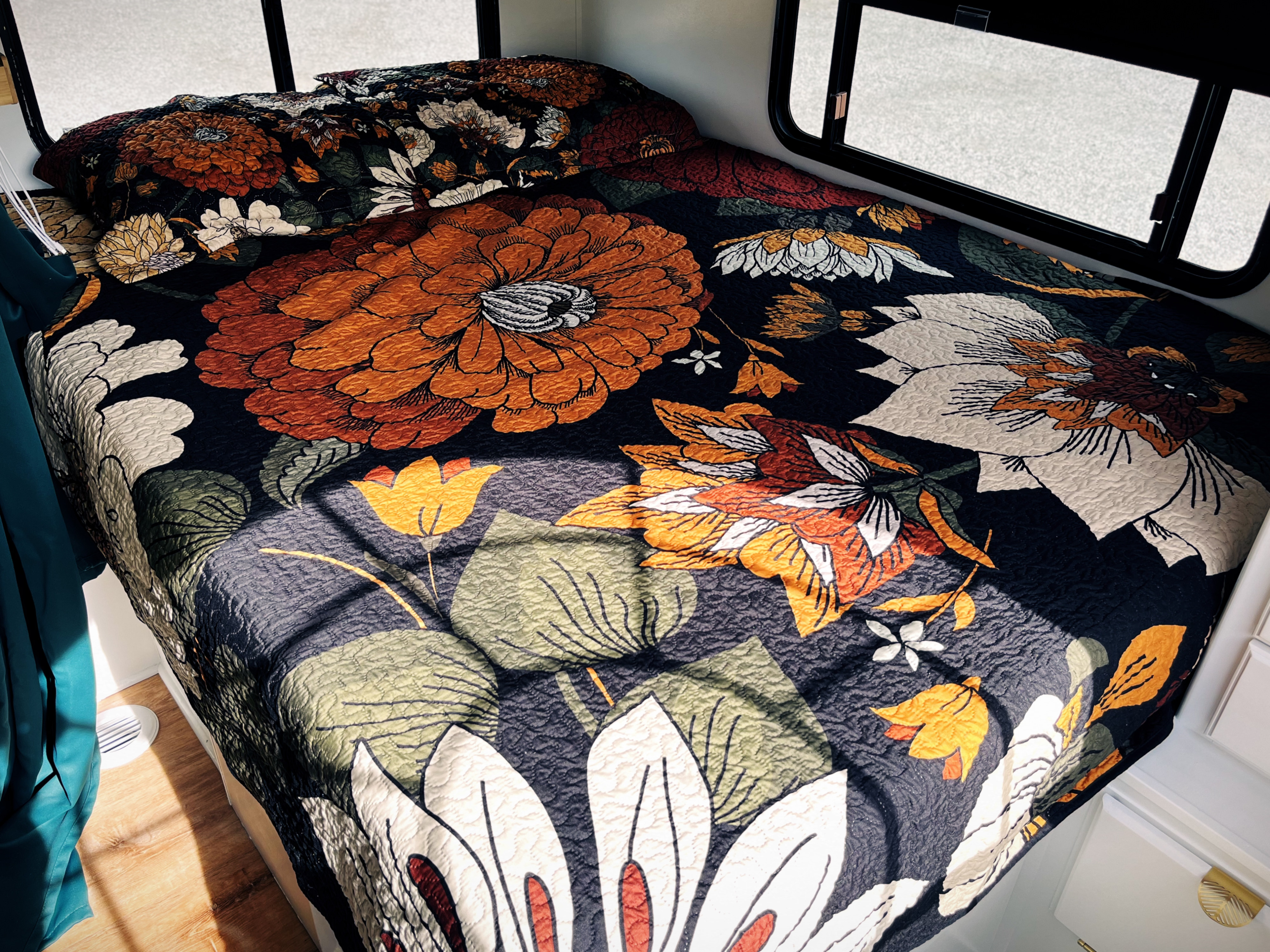 Cozy RV rental bed with a vibrant floral comforter featuring orange, white, and green flowers on a dark background.. Coachmen Freelander Premier 2006