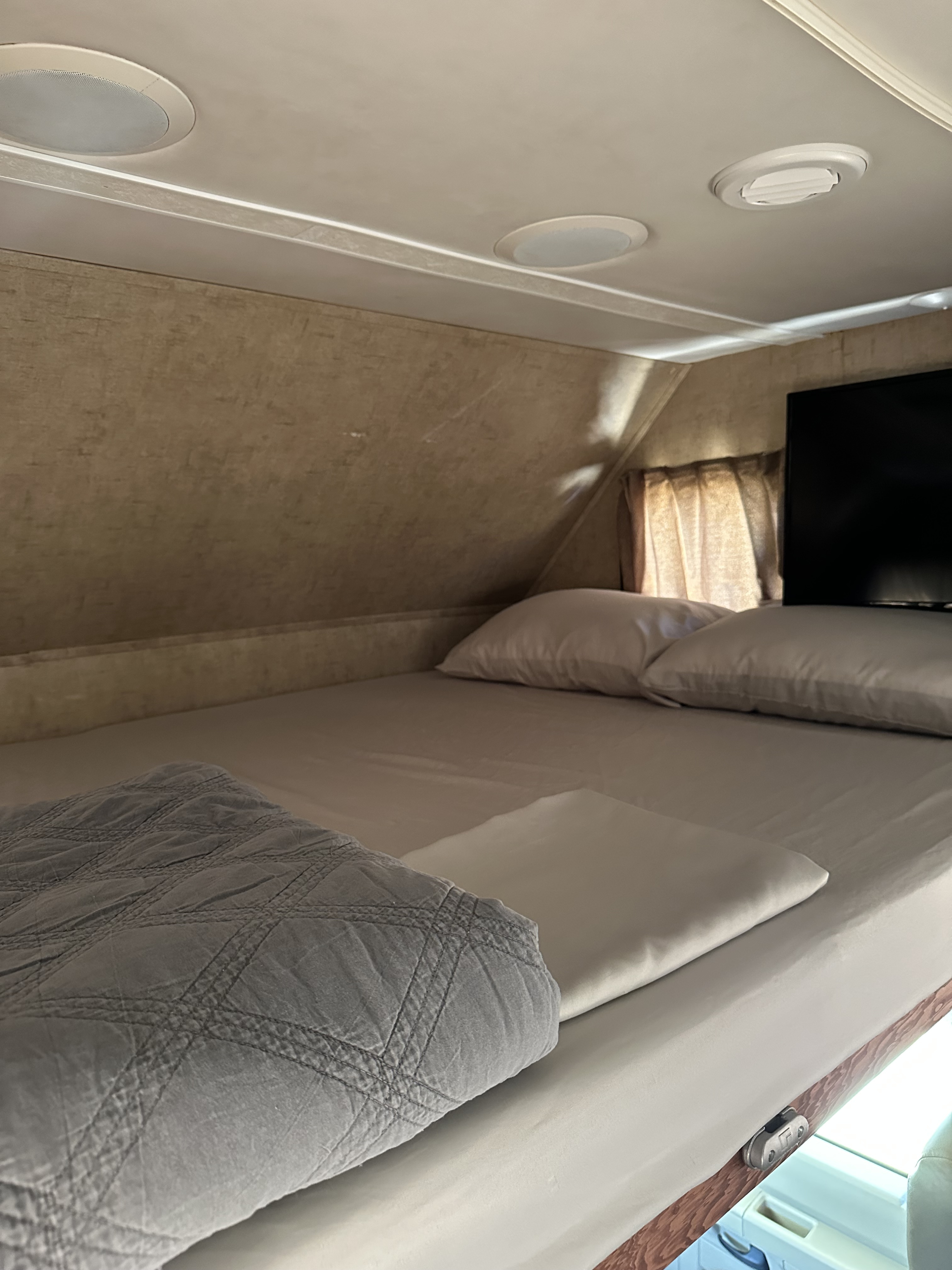 An inviting RV rental sleeping area: a neat bed with fresh linens, pillows, gray quilted blanket. Ceiling lights, vent, and TV are visible.. Forest River Forester 2861DS 2016
