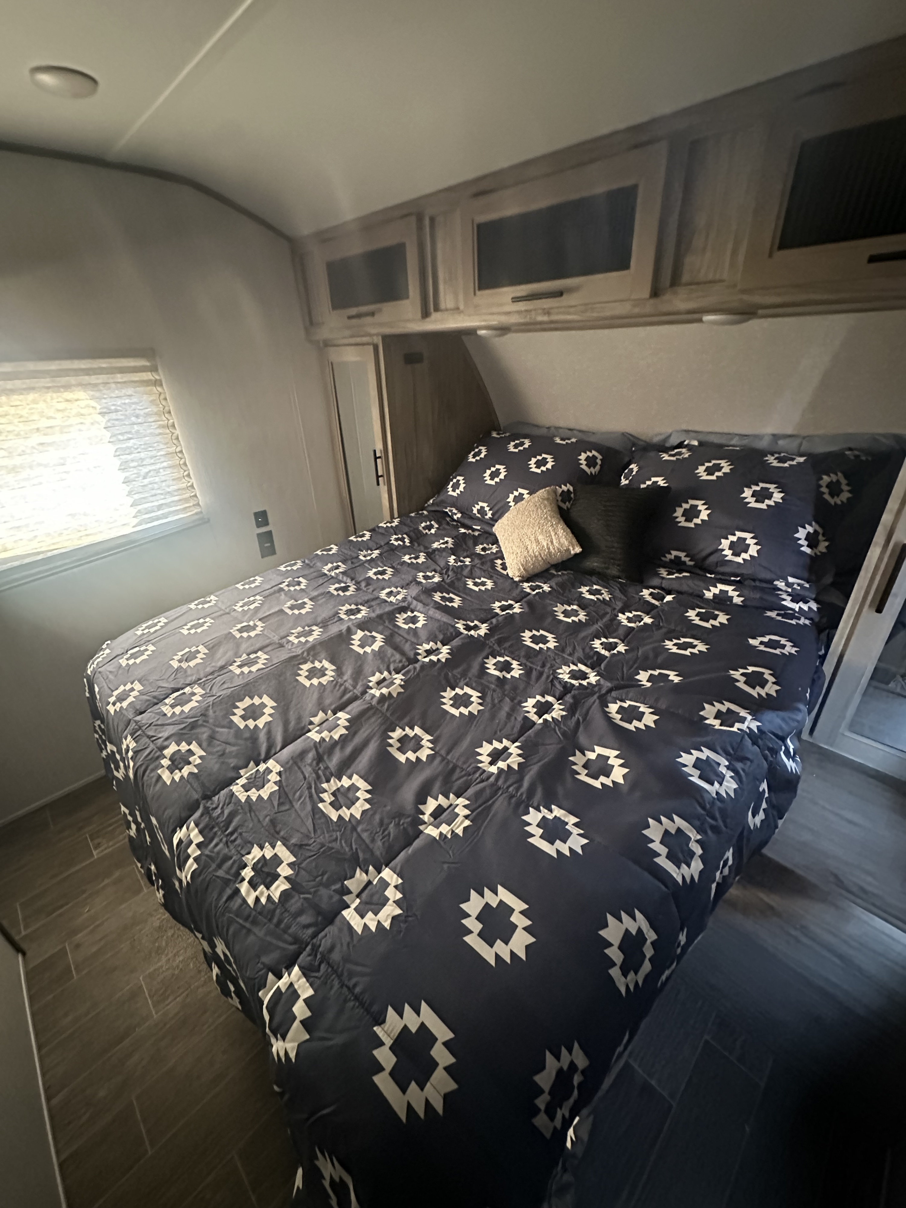 Cozy RV rental bedroom with patterned comforter, overhead cabinets, a window, and wood-look flooring.. Forest River Cherokee Alpha Wolf 2021