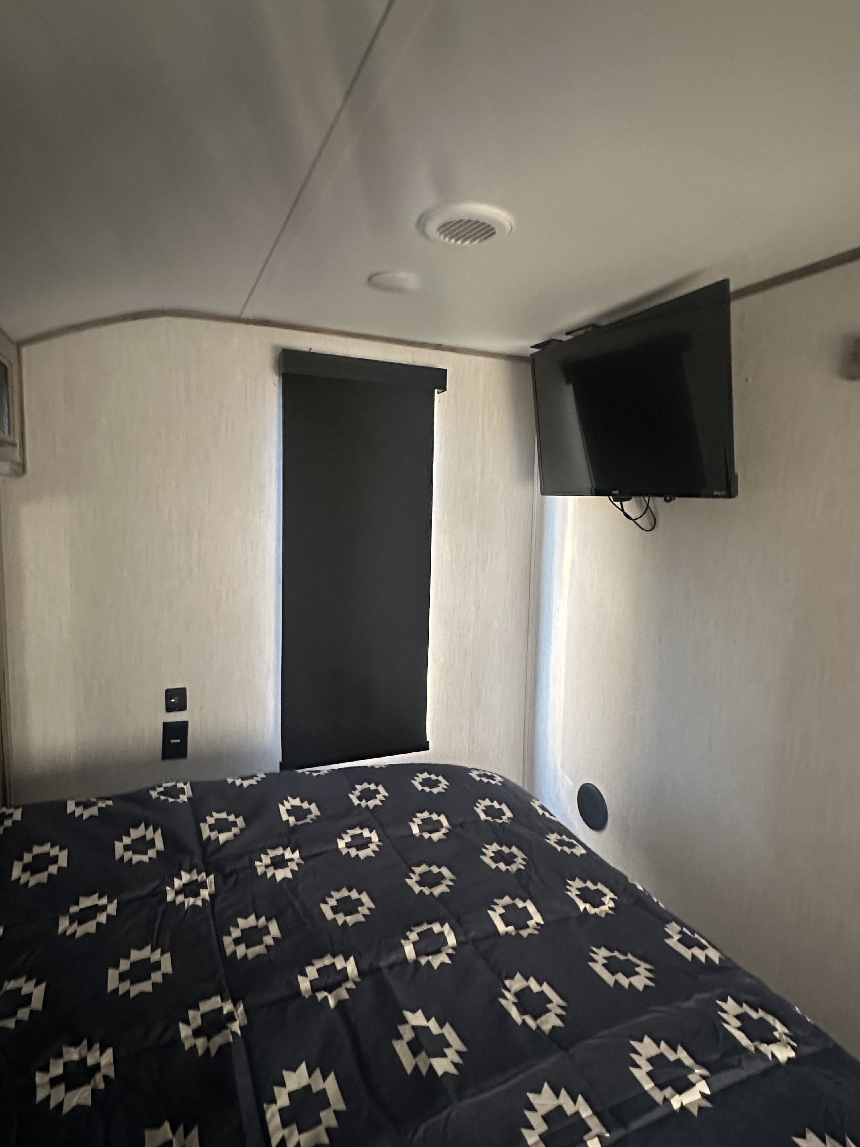 Inside an RV rental, this cozy bedroom features a patterned bedspread, wall-mounted TV, and window shade.. Forest River Cherokee Alpha Wolf 2021