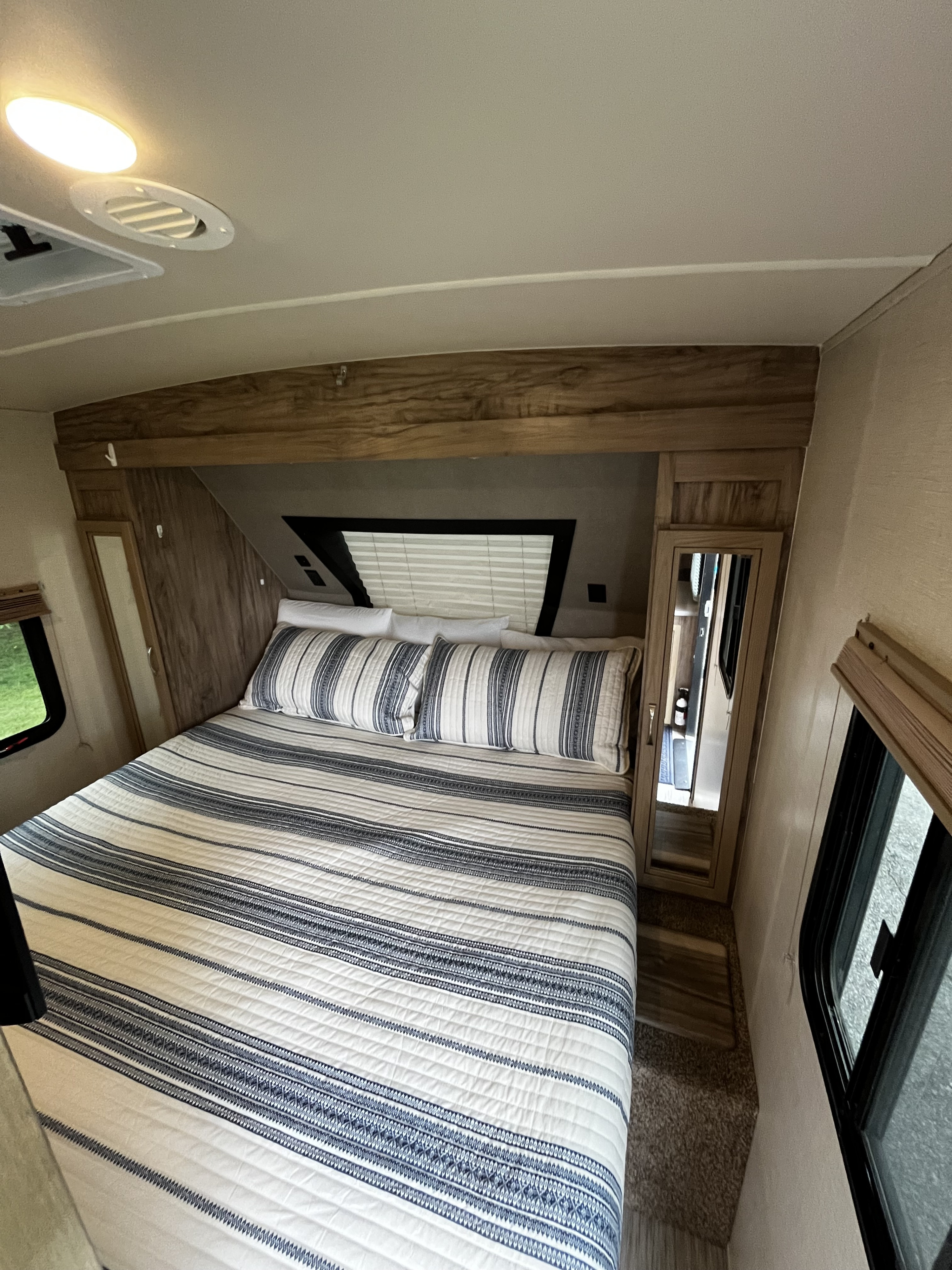 Cozy RV rental bedroom featuring a bed with blue and white striped bedding, wooden storage, and bright windows.. Forest River Palomino Solaire 2021