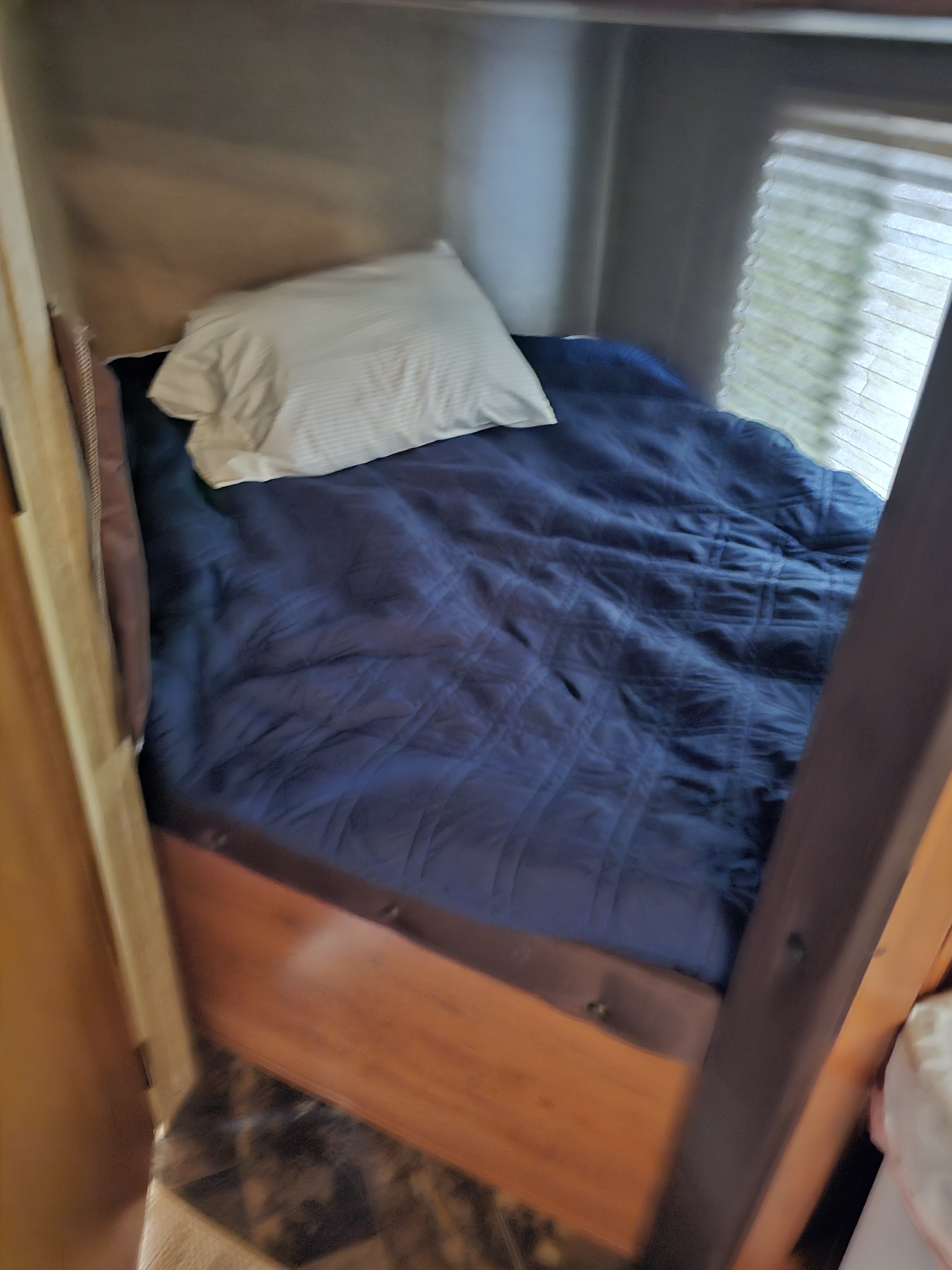 Compact RV rental bedroom with blue comforter & white pillow on a built-in bed, featuring a window with blinds.. Forest River Cherokee Grey Wolf 2016