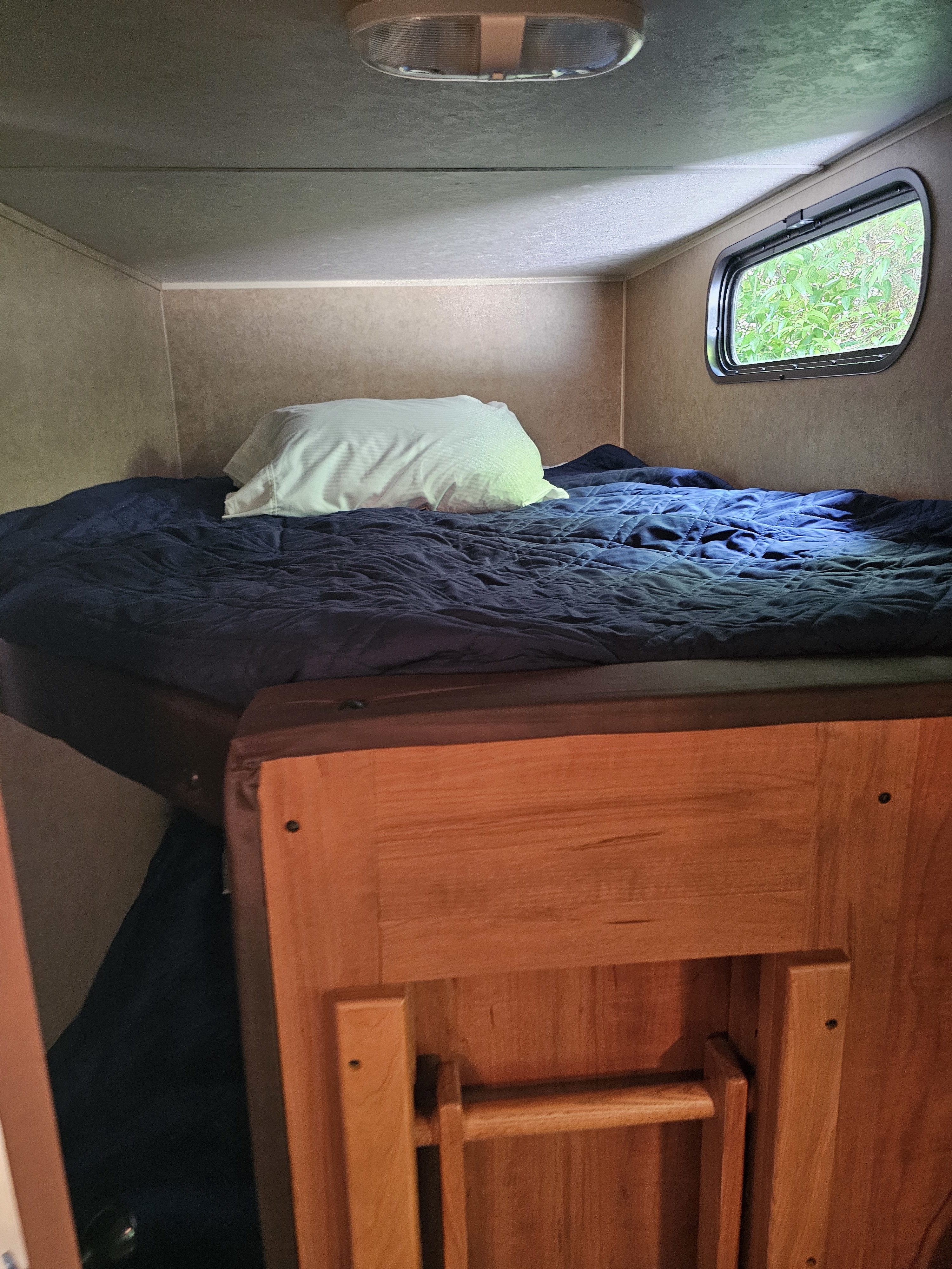 Cozy RV rental sleeping area with a bed, blue comforter, white pillow, overhead light, and window.. Forest River Cherokee Grey Wolf 2016