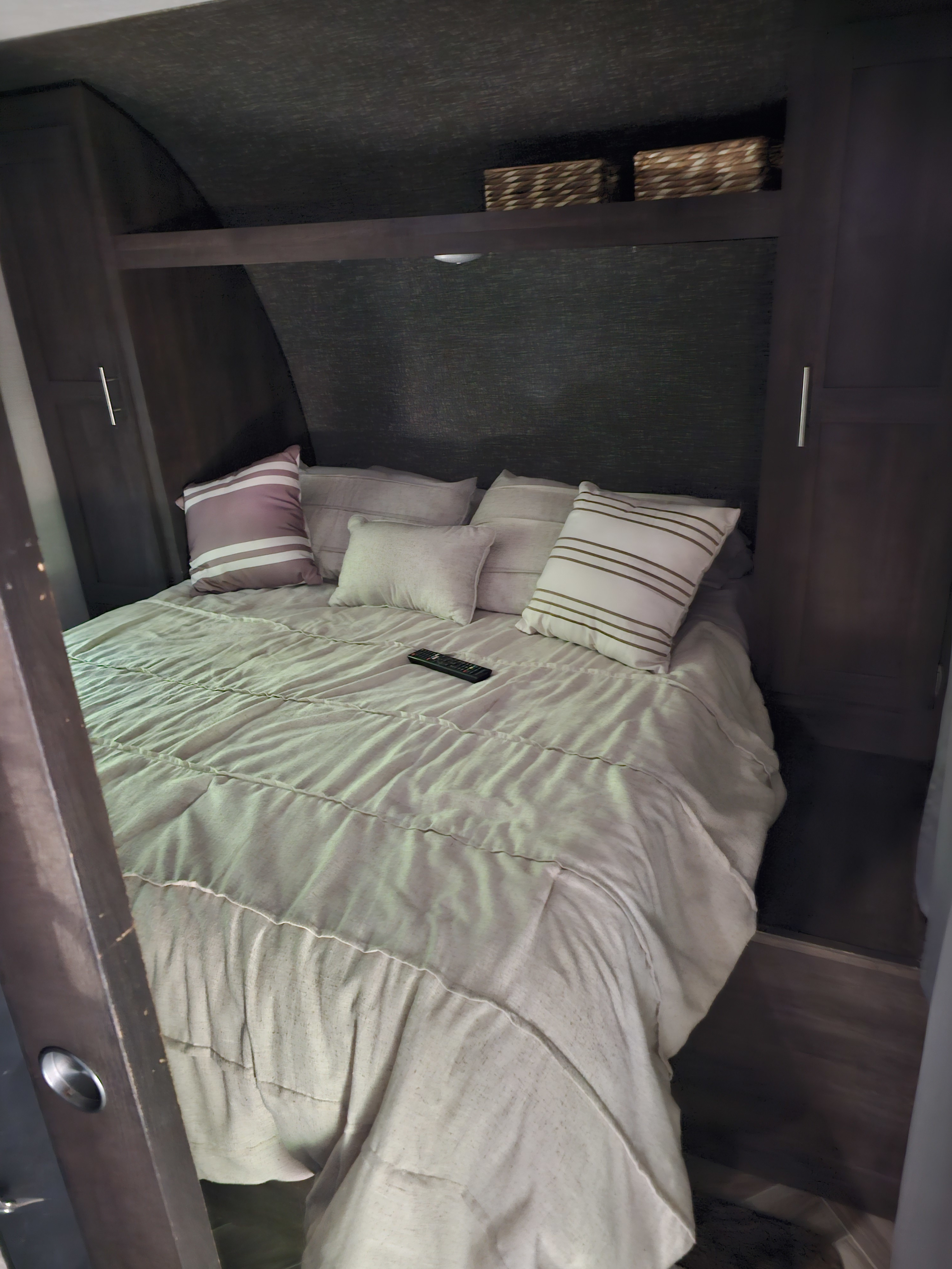 Inside an RV rental: a compact and cozy bedroom with a comfortable bed, pillows, overhead storage, and cabinet space.. KZ Sportsman 2021