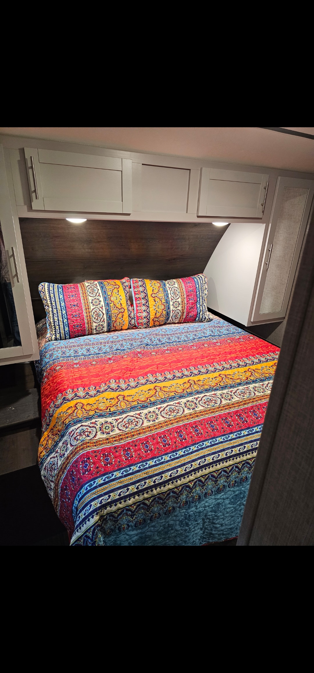 Cozy RV rental bedroom with vibrant, patterned quilt, overhead cabinets, and reading lights.. Keystone RV Bullet Ultra Lite 2019