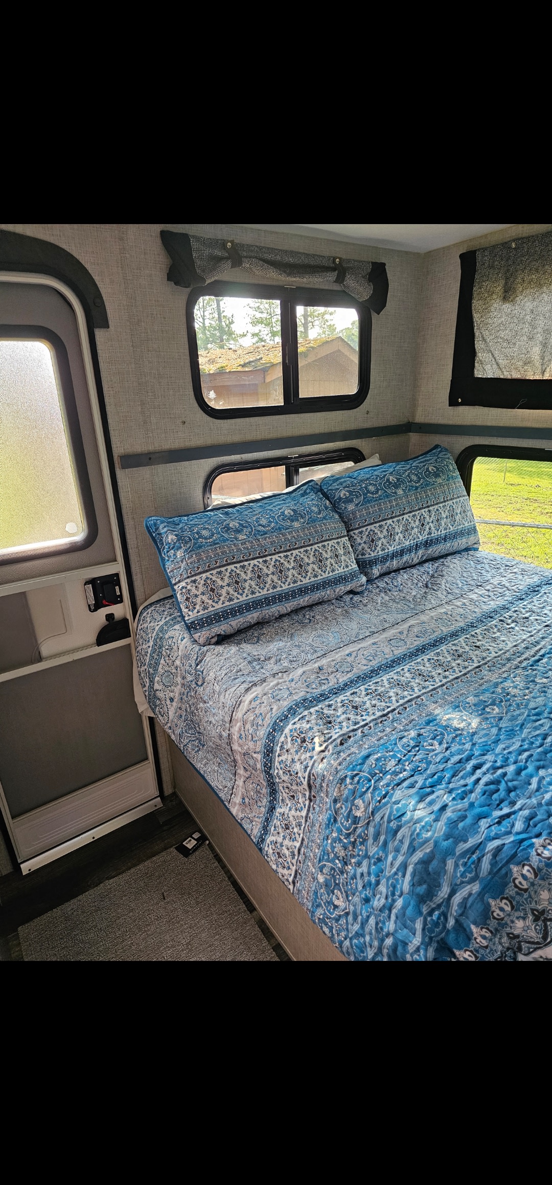 Cozy RV rental bedroom with patterned blue bedding, natural light from windows, and an open door.. Keystone RV Bullet Ultra Lite 2019