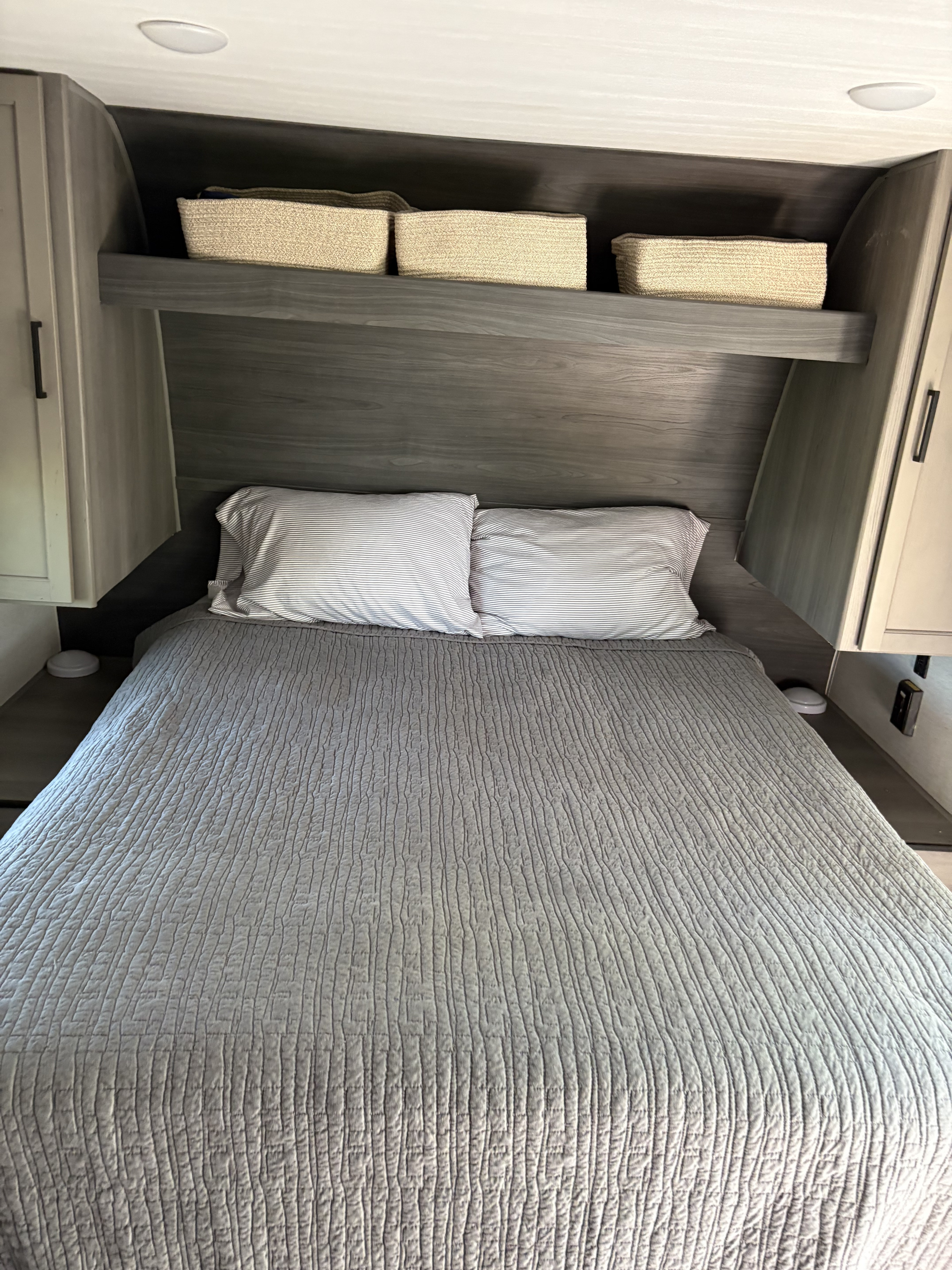 Cozy RV rental bedroom featuring a neatly made bed with gray quilt & striped pillows, plus functional overhead storage.. Keystone RV Hideout Sport 2024