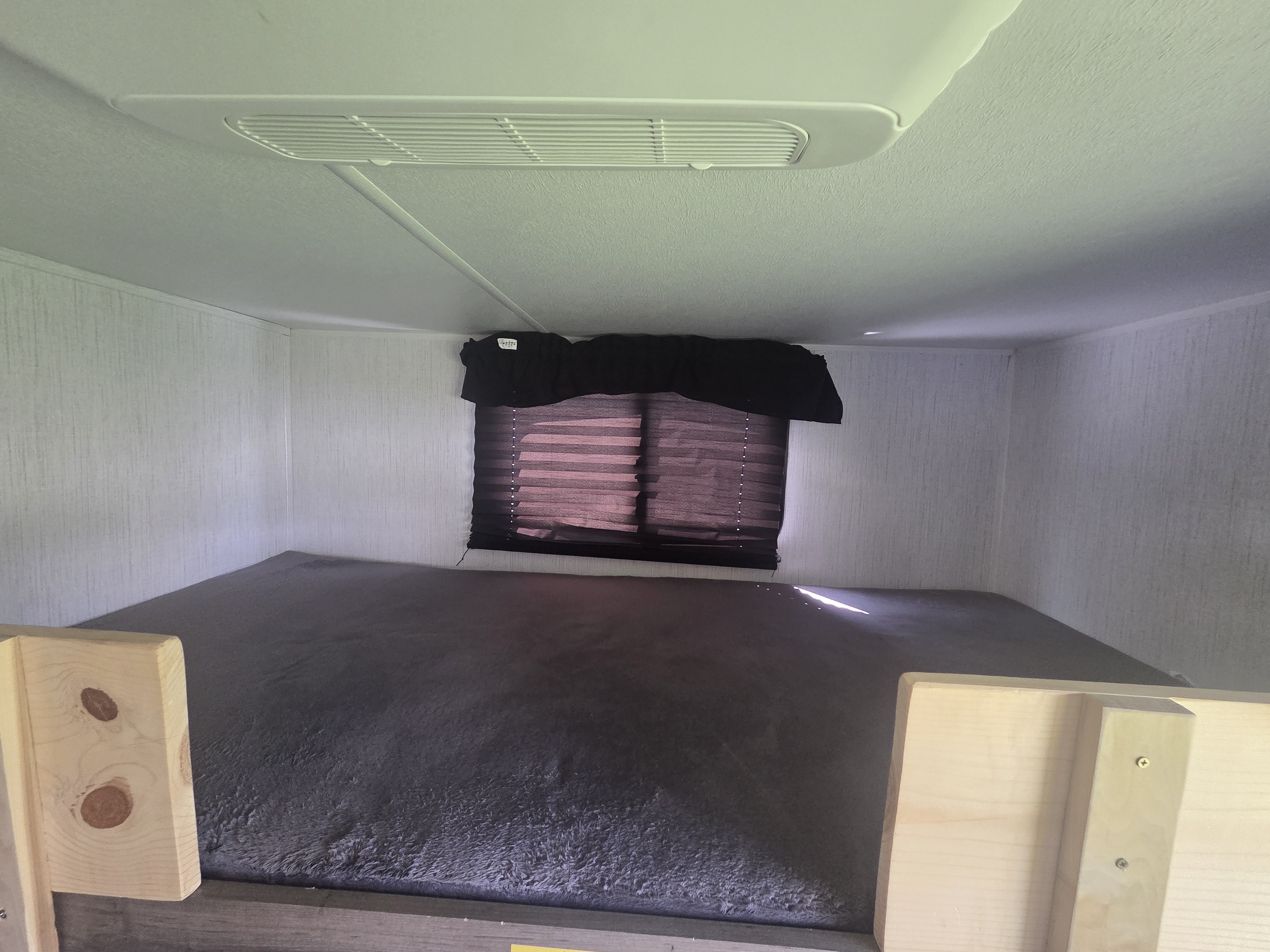 RV rental bunk bed with AC vent, window blinds, and dark bedding, offering a cozy sleeping area.. Heartland RVs Pioneer 2023