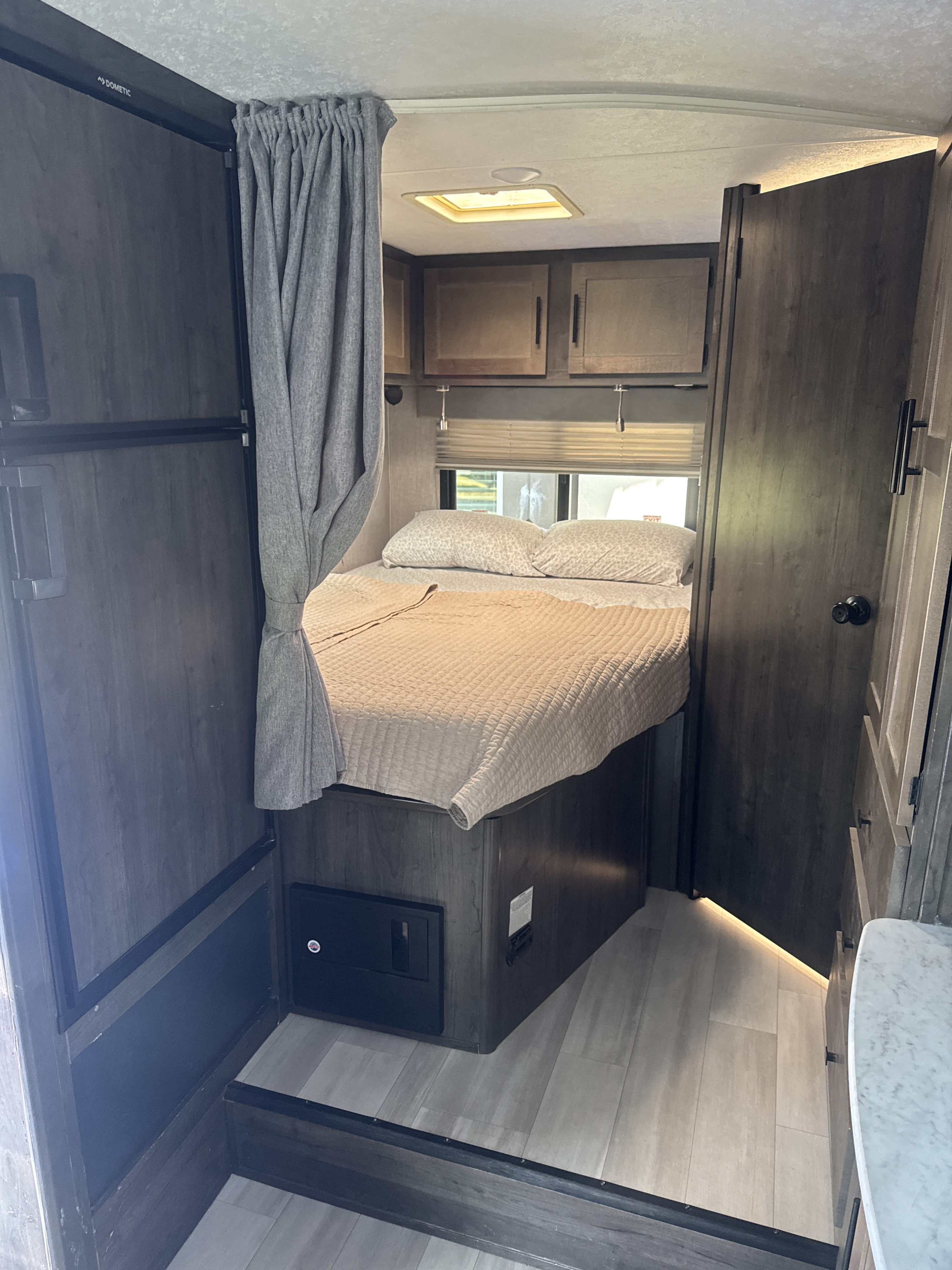 Inside this **RV rental**: a compact bedroom with a cozy bed, overhead storage, and a Dometic fridge for comfortable travel.. Coachmen Leprechaun 23CB 2022