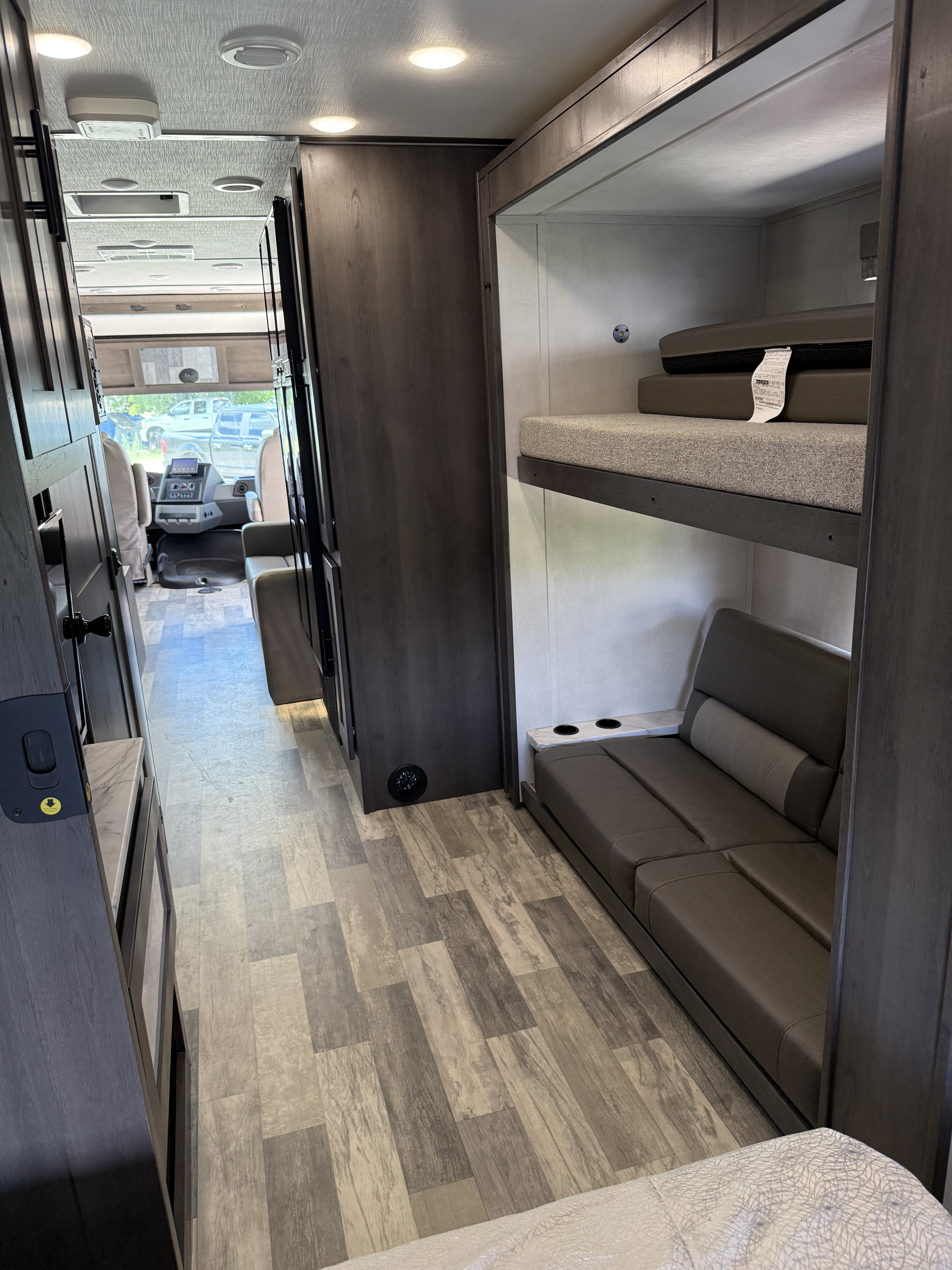 Interior of a modern RV rental: a hallway leads to the driver's area, with bunk beds over a sofa on the right.. FR3 32D 2023