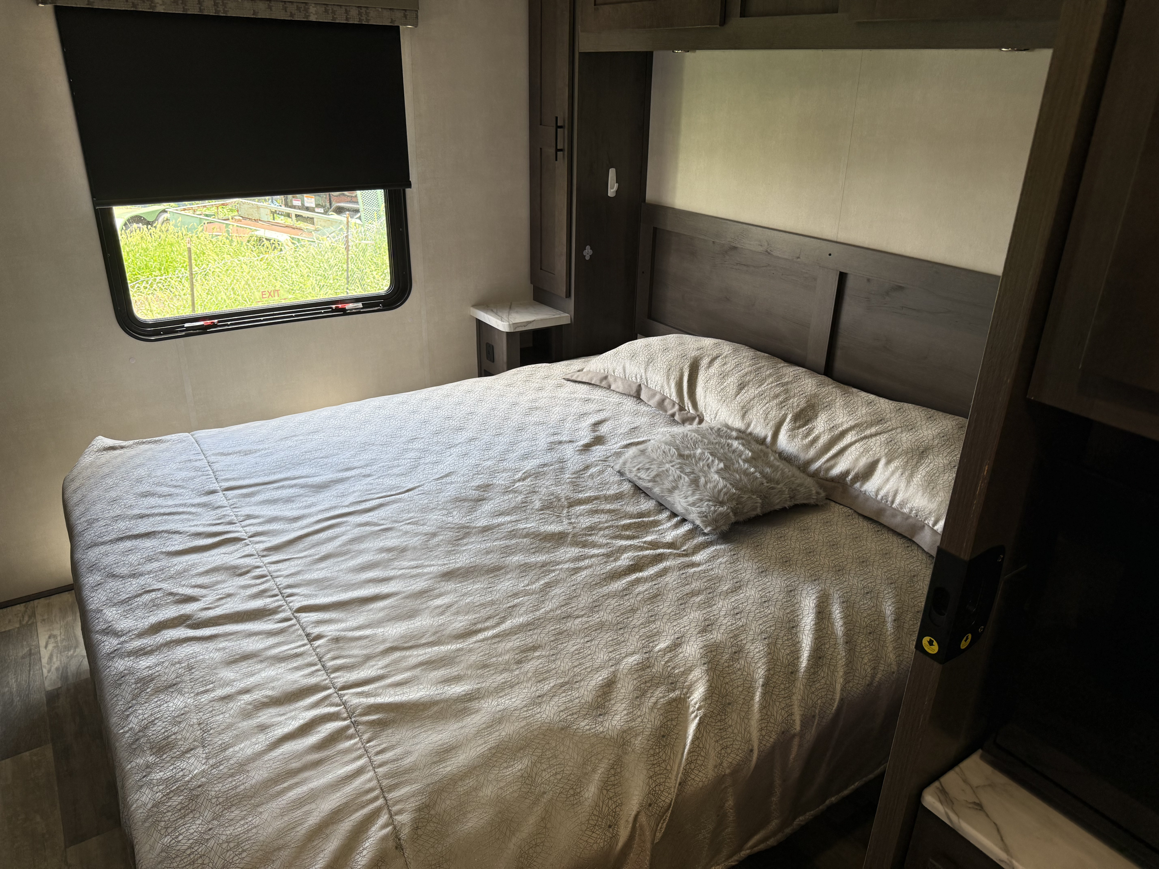 Cozy RV rental bedroom with a bed, patterned linens, a window with a blackout shade, and built-in storage.. FR3 32D 2023