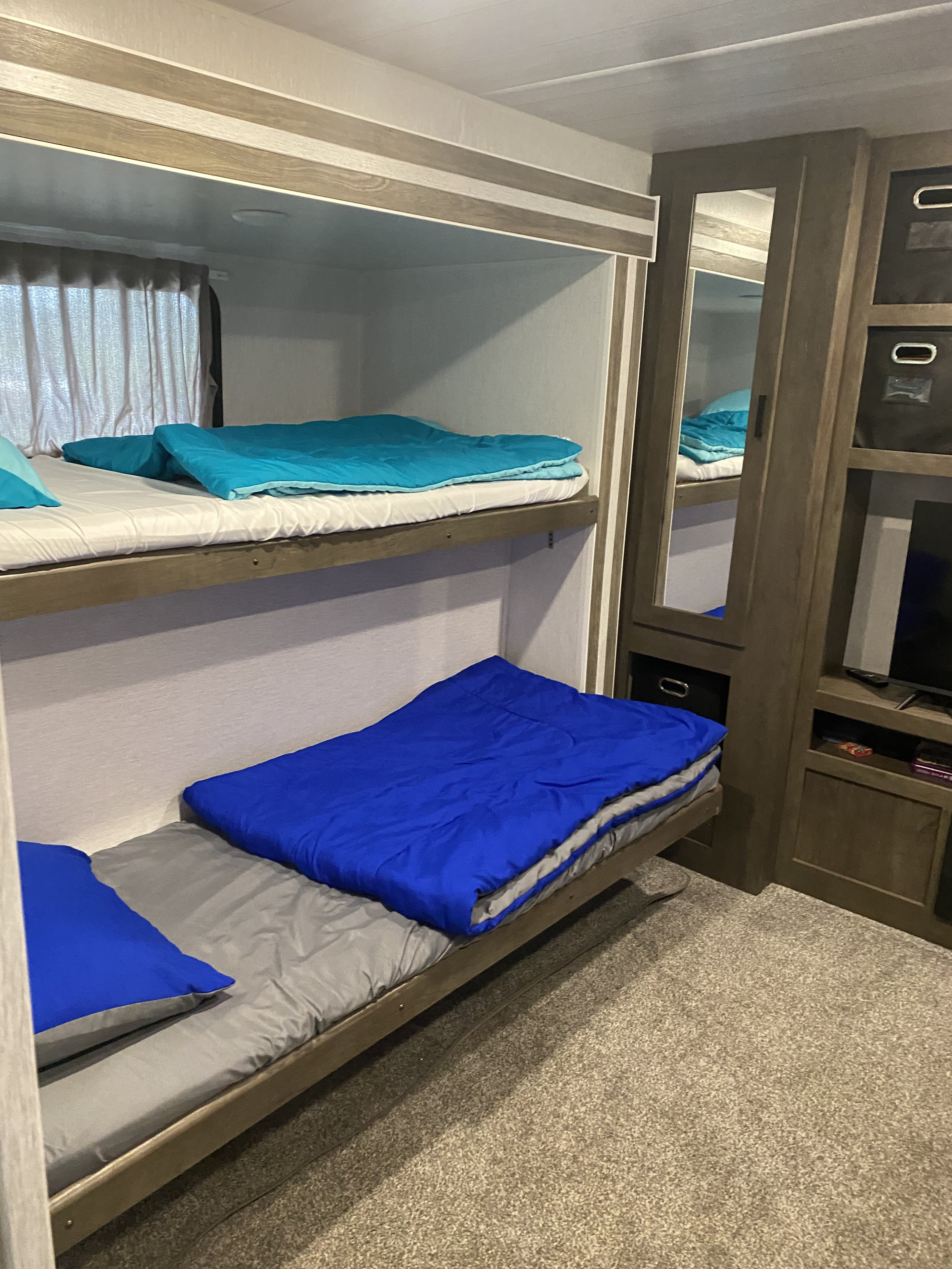 This RV rental's interior features stacked bunk beds with blue and teal bedding, perfect for compact travel.. Forest River Wildwood 2022