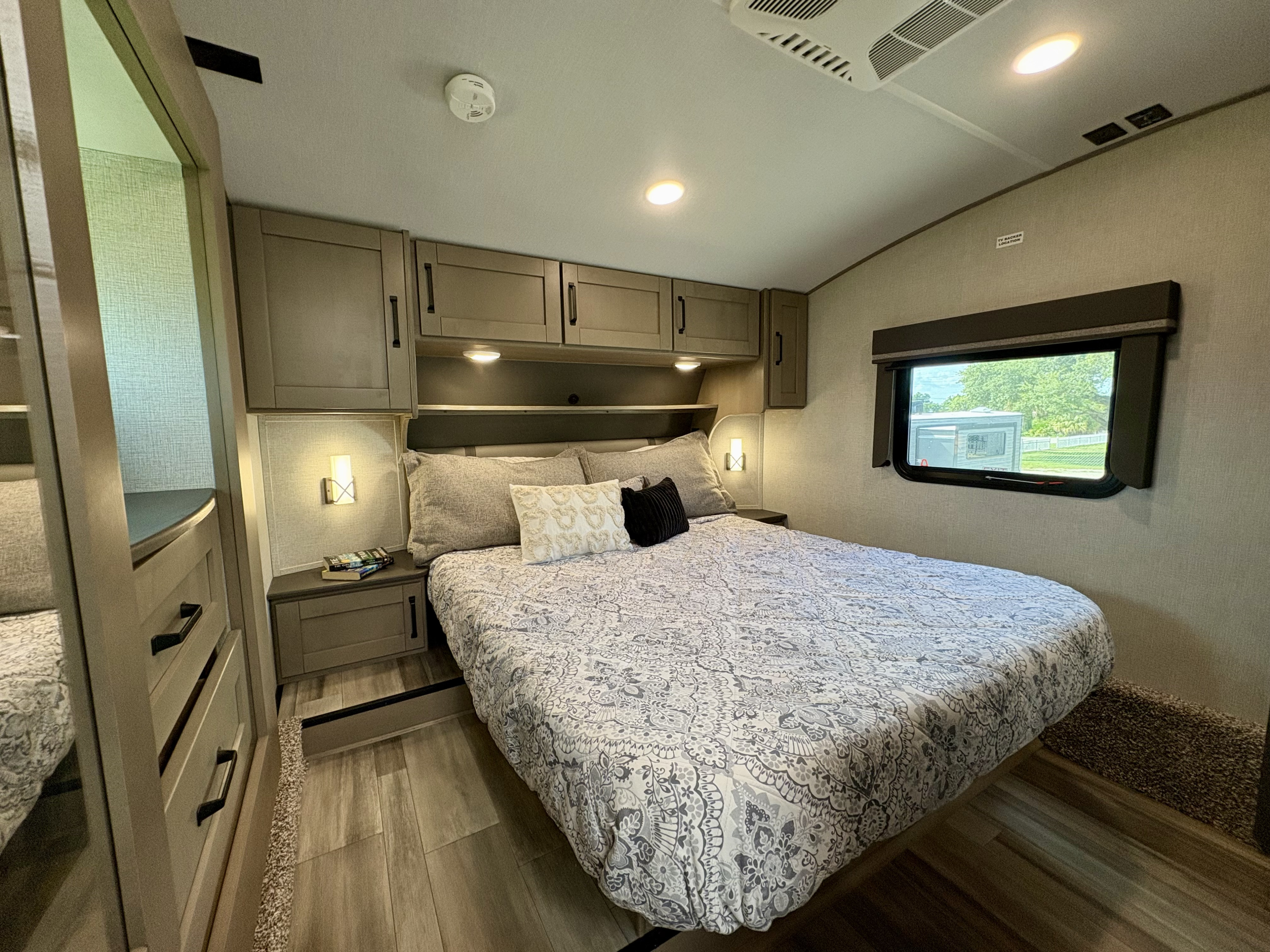 Modern RV rental bedroom featuring a large bed, nightstands, overhead storage, and a bright window. Ideal for comfortable travel.. Grand Design Reflection 2023