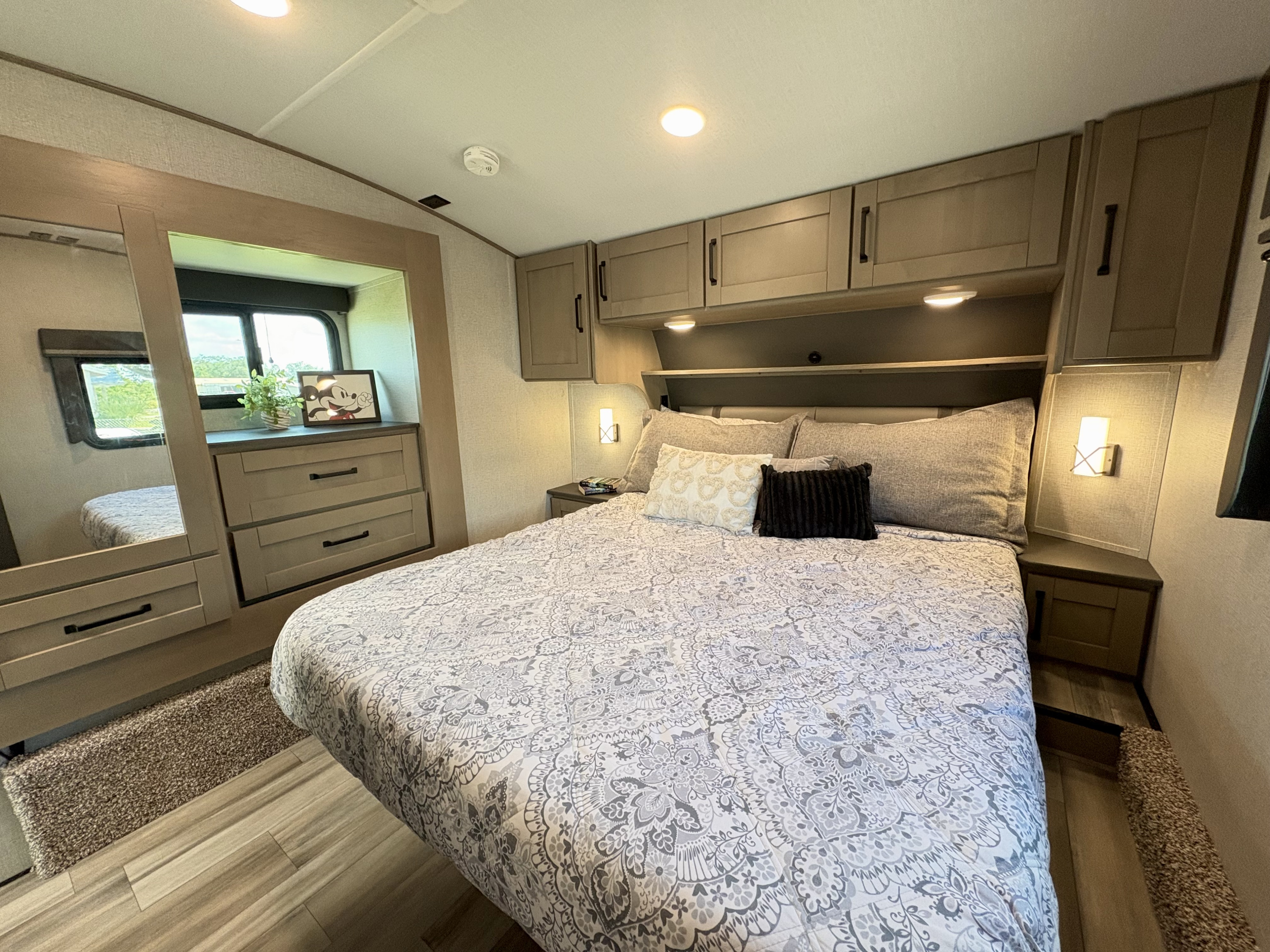Experience comfort in this modern RV rental bedroom, featuring a large bed, ample storage, and natural light from wide windows.. Grand Design Reflection 2023