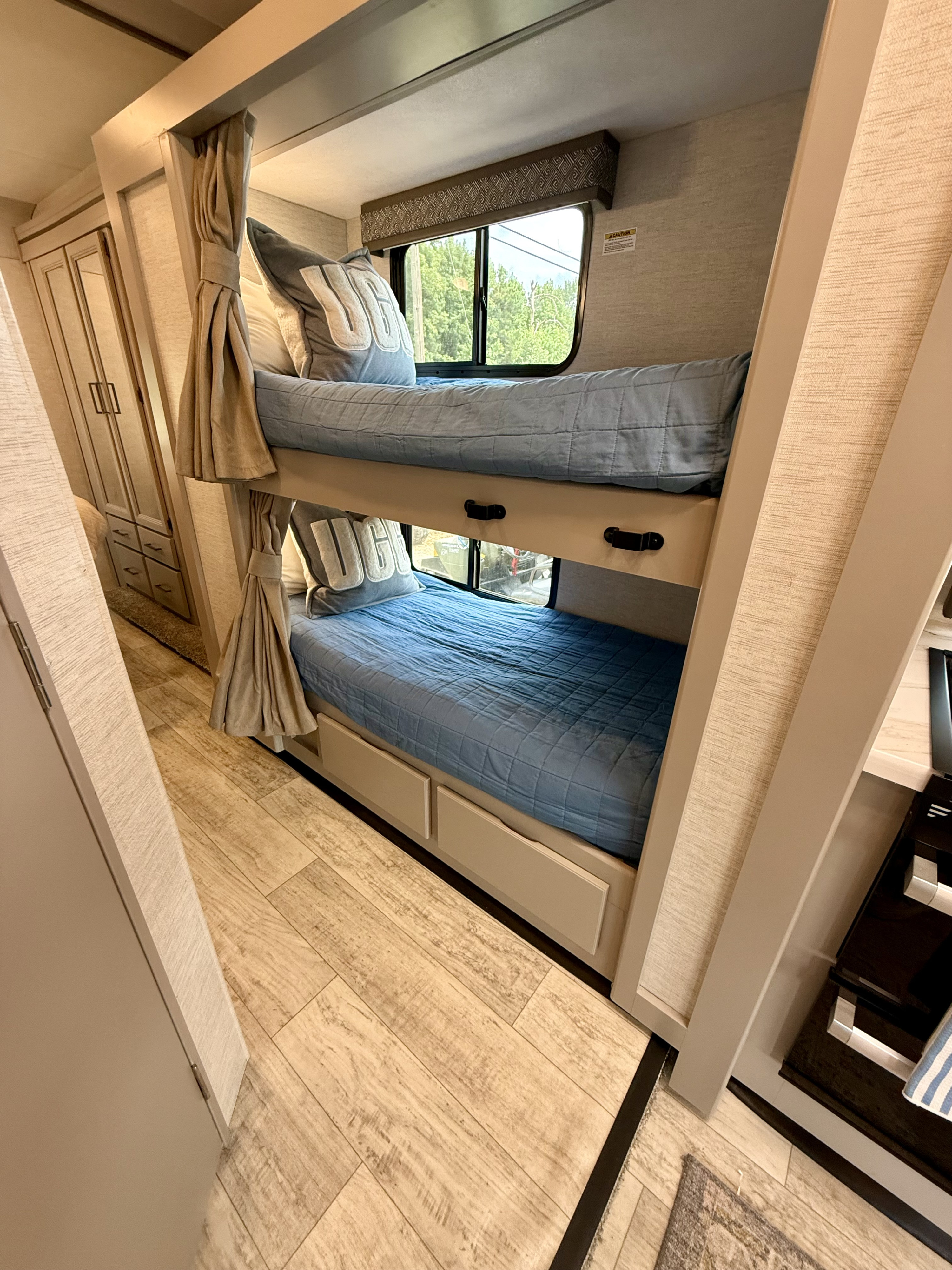 Cozy bunk beds in an RV rental, perfect for families. Features blue bedding, window views, and under-bed storage drawers.. Thor Chateau 2024