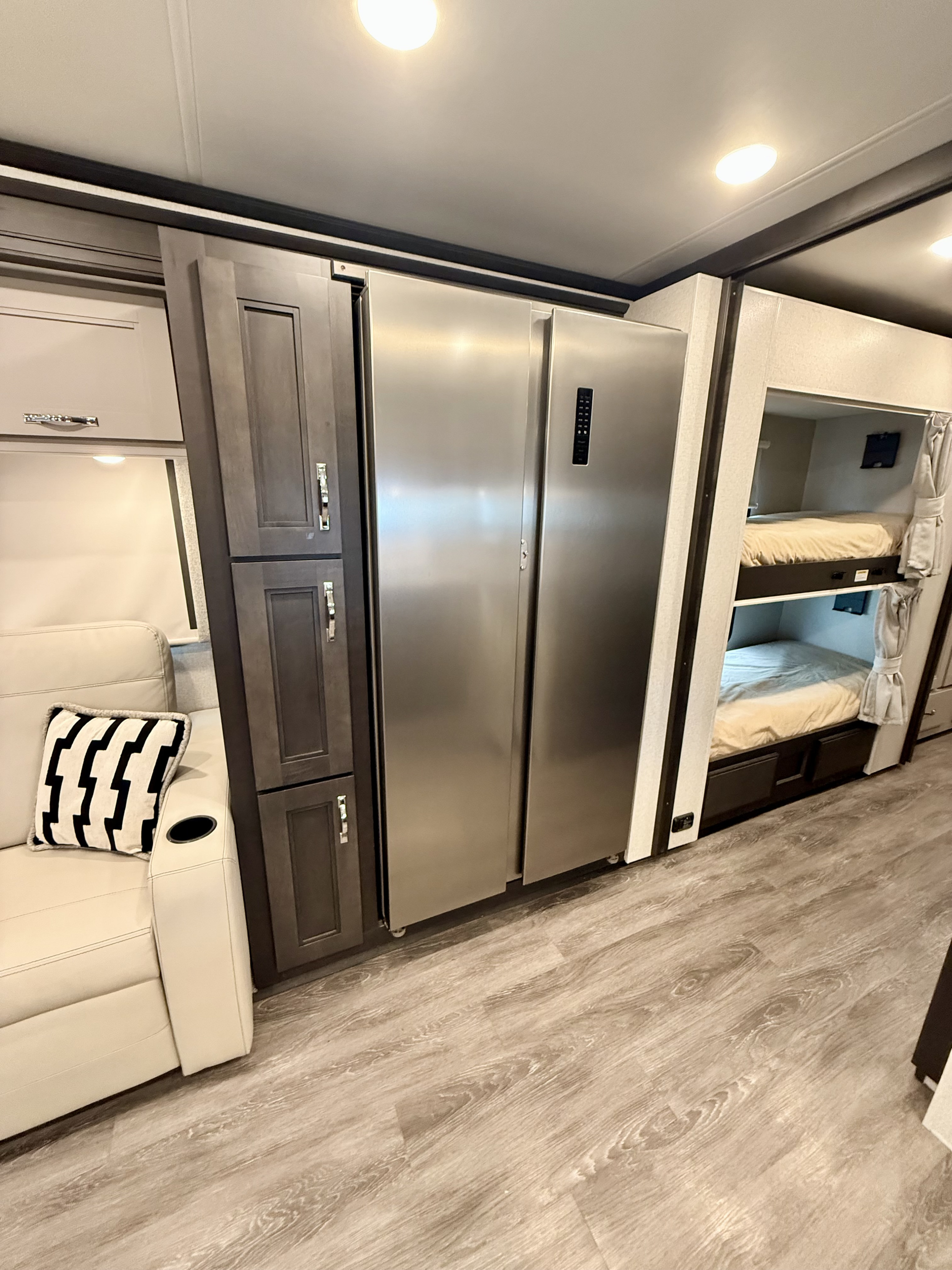 RV rental interior showcases a full-size refrigerator, bunk beds with curtains, and a light-colored sofa.. Thor Riviera 2024