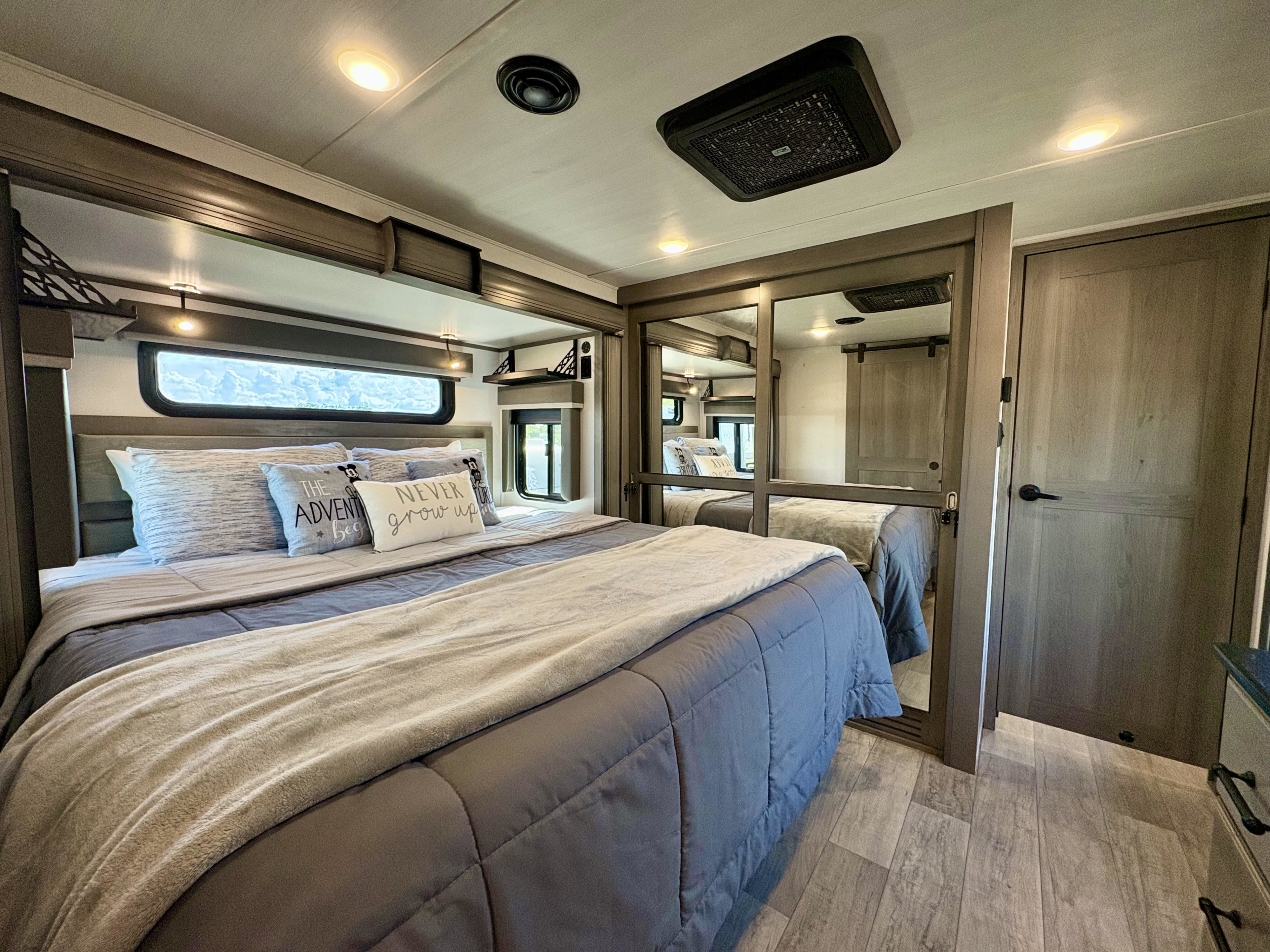 Modern RV rental bedroom with a large bed, mirrored closet, and sleek lighting, offering comfort and style.. Keystone Montana 2023