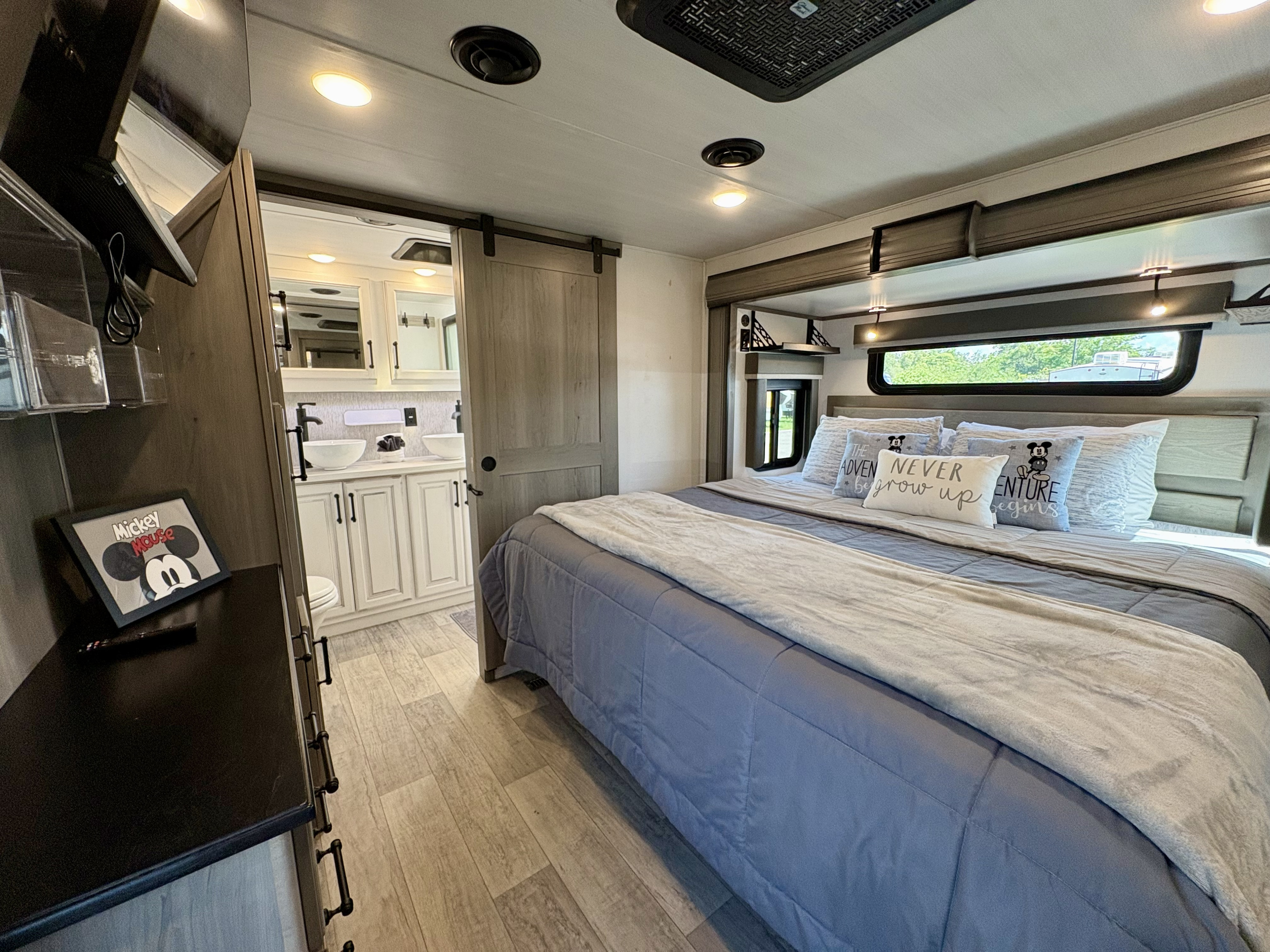 Spacious RV rental bedroom with a large bed, TV, and a sliding door revealing a modern bathroom with dual sinks.. Keystone Montana 2023