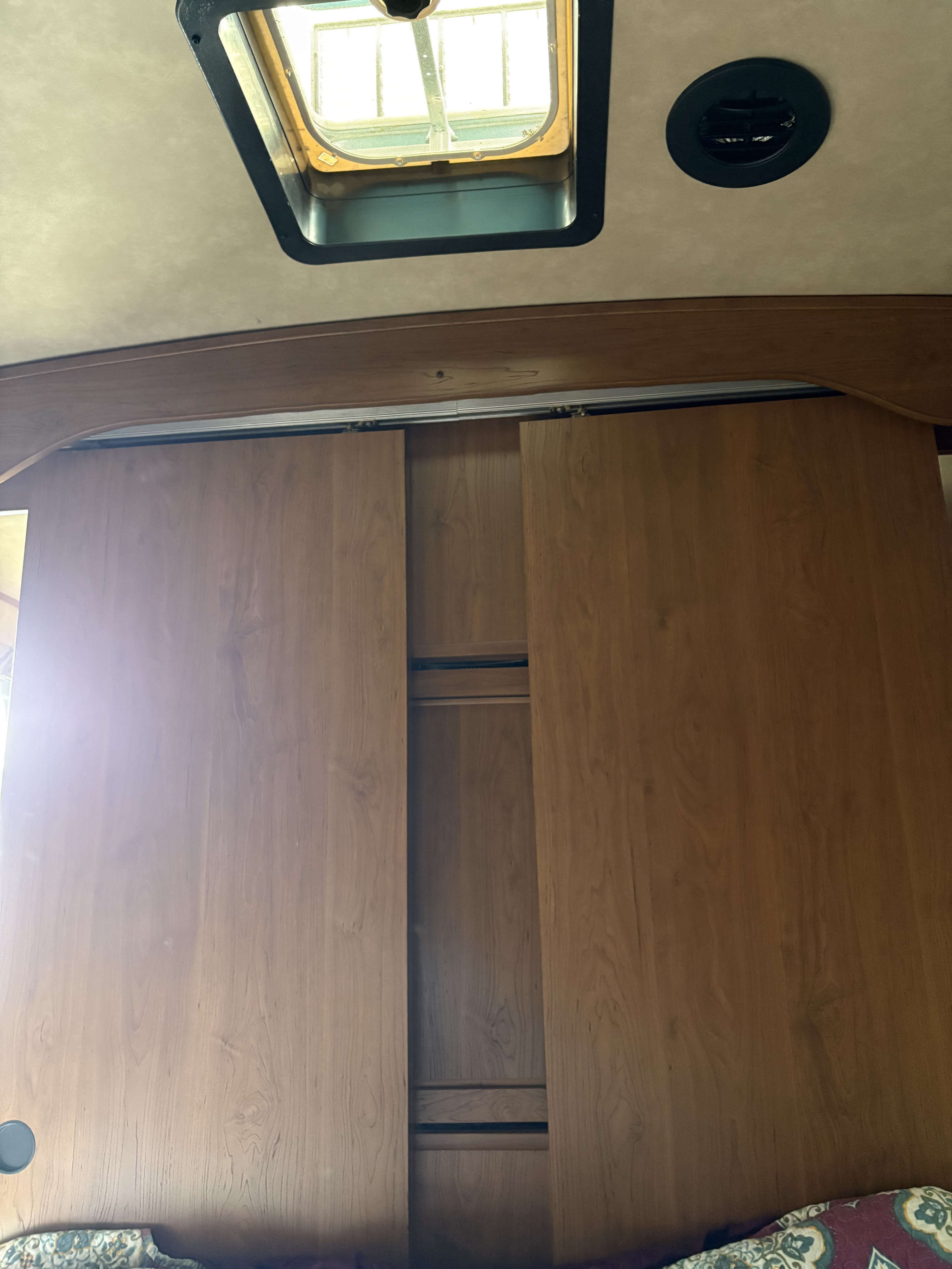 Inside an RV rental: Wooden sliding closet doors, partially open to reveal storage, below an overhead skylight and air vent.. Crossroads RV Sunset Trail Super Lite 2016