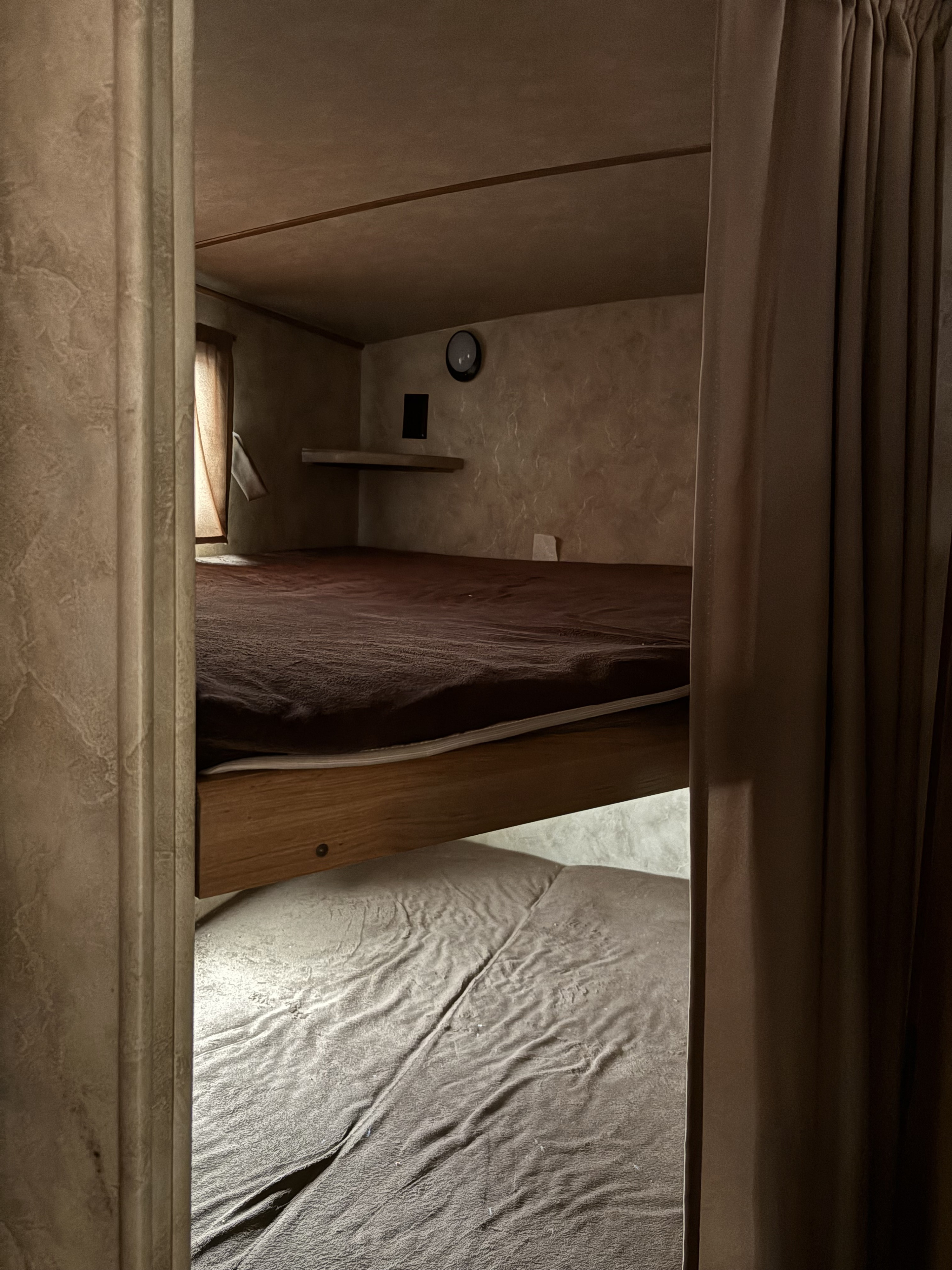 Cozy bunk beds inside an RV rental, featuring brown and grey bedding, textured walls, and privacy curtains for compact travel sleep.. Crossroads RV Sunset Trail Super Lite 2016