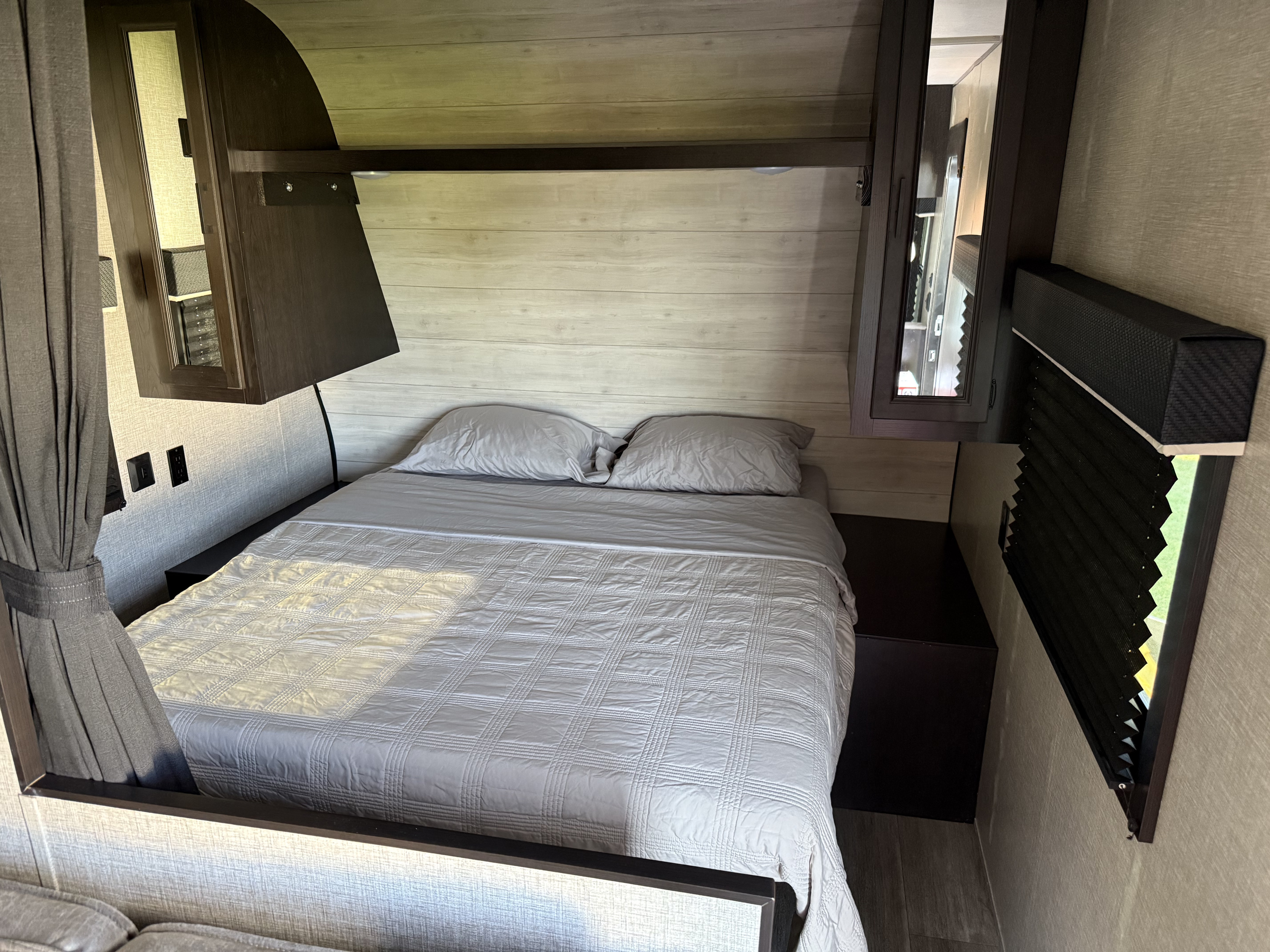 Inside an RV rental: a neatly made bedroom with a light gray bed, overhead storage, and window with blinds.. Jayco Jay Flight SLX 2022