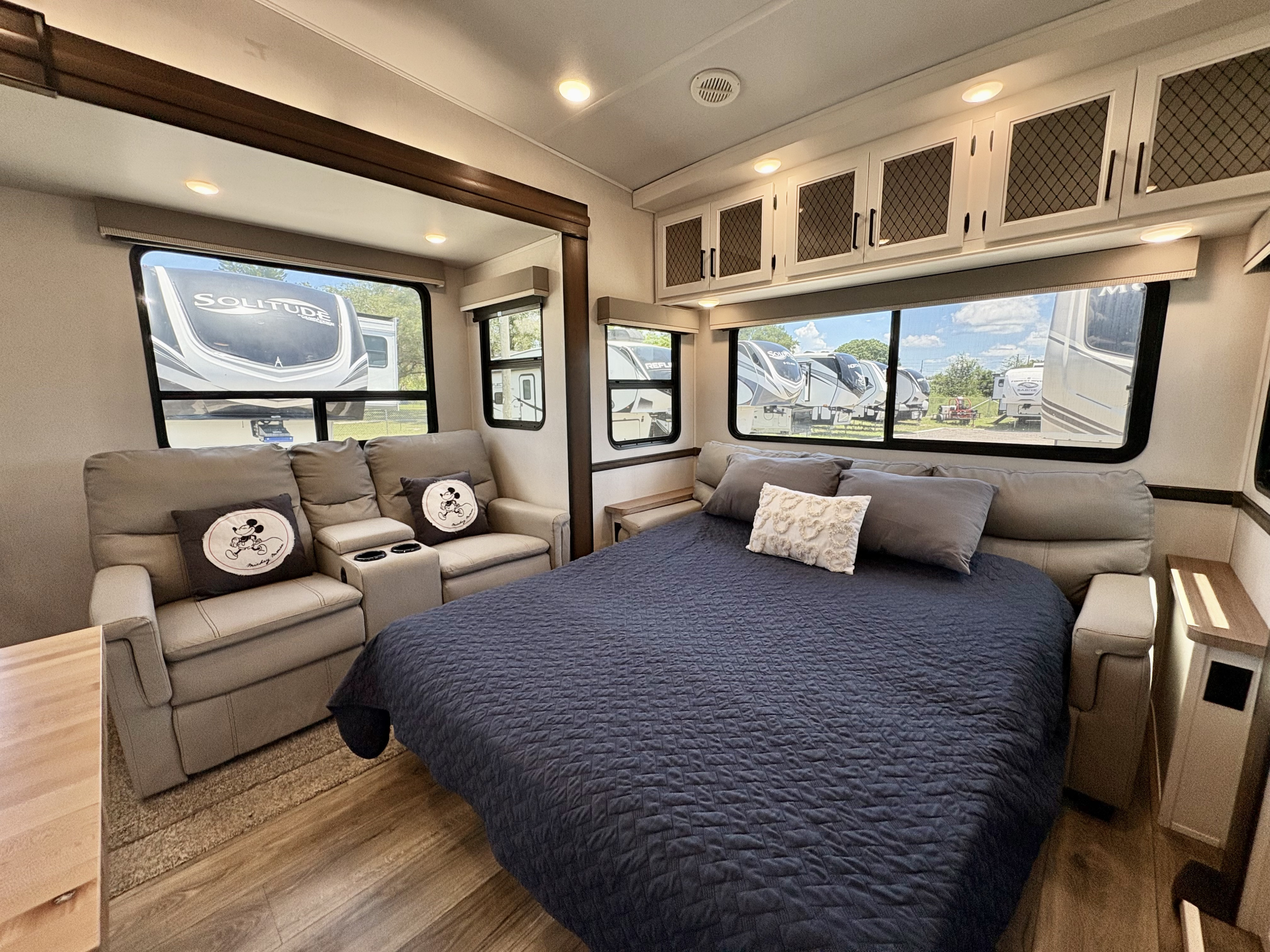 Explore this modern RV rental bedroom/living space with a large bed, comfy recliners, overhead cabinets, and bright windows.. Forest River Crusader 2022