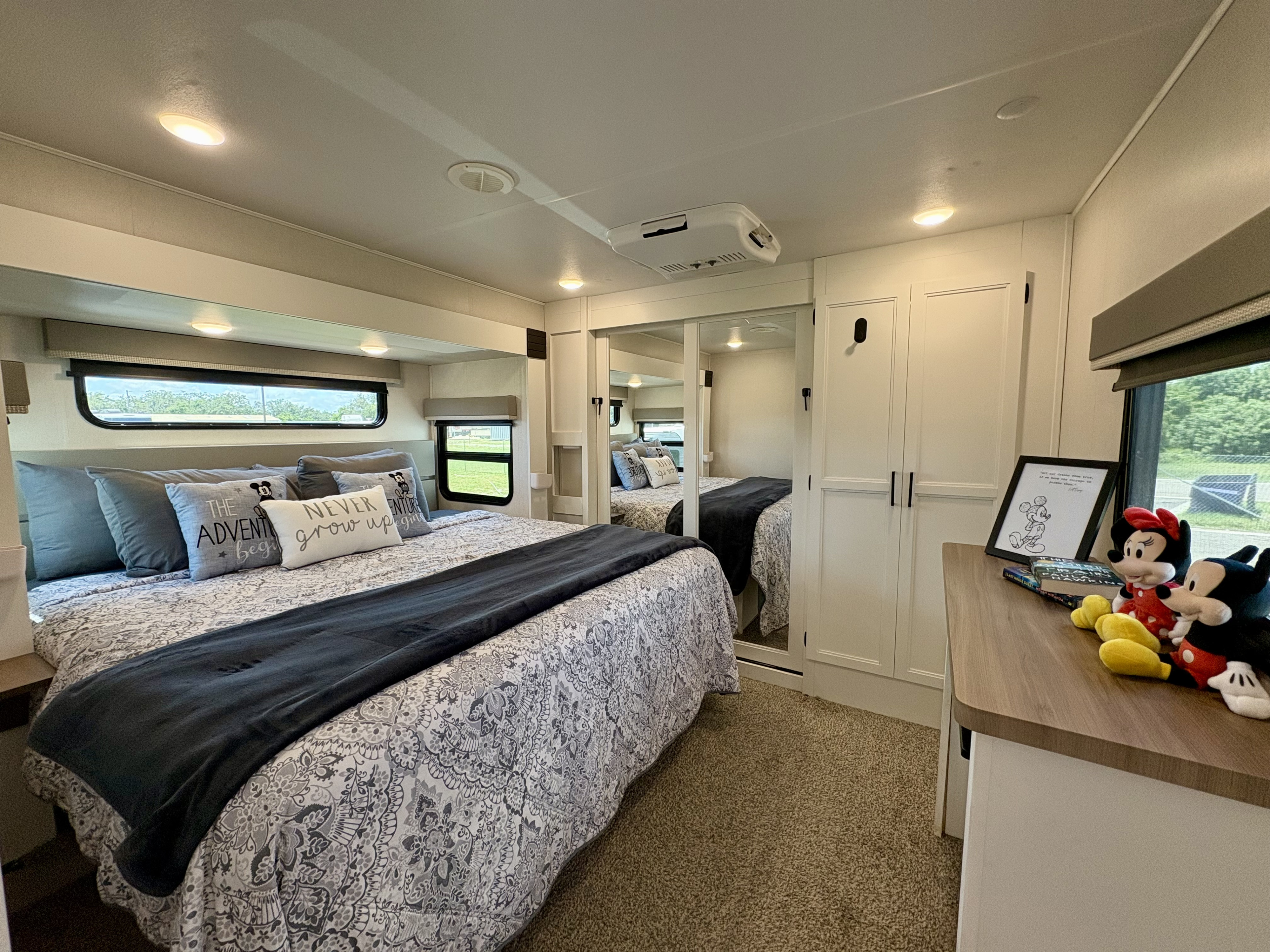 Cozy RV rental bedroom featuring a patterned queen bed, Mickey & Minnie decor, mirrored closets, and bright windows.. Forest River Crusader 2022