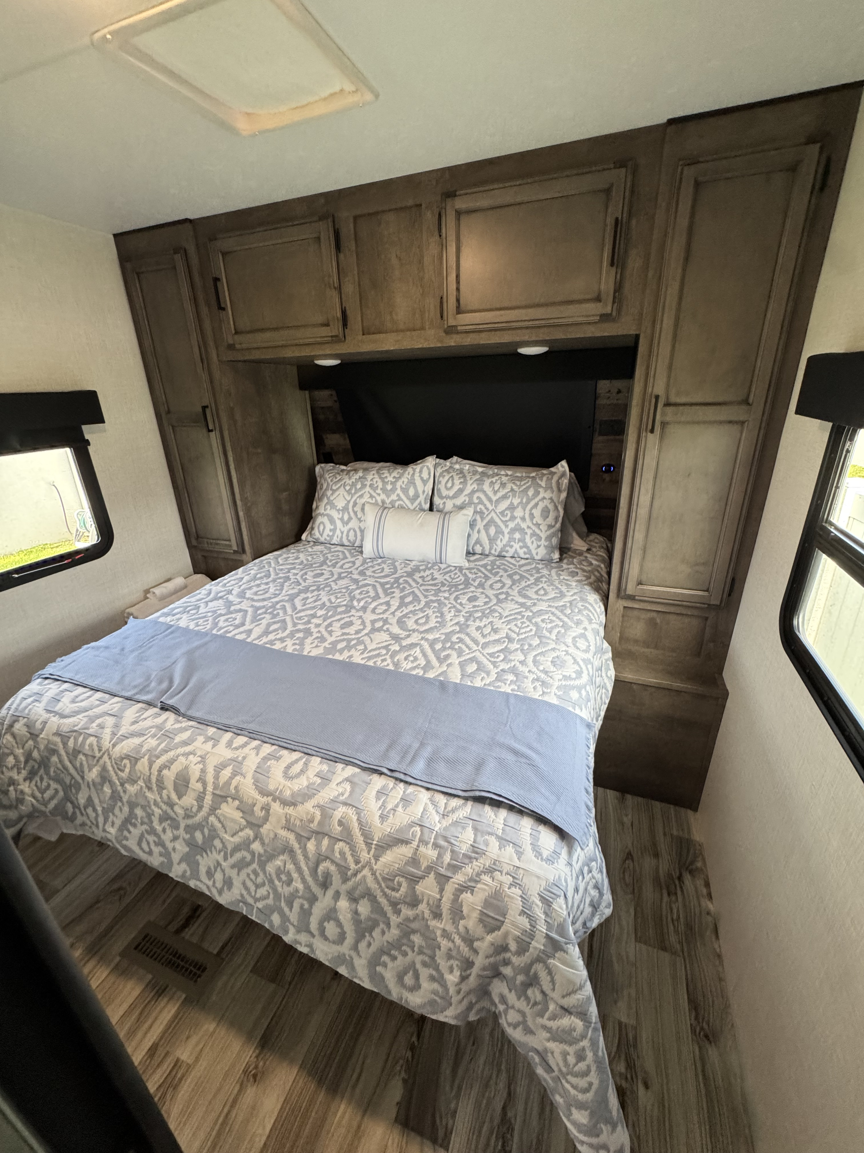 Comfortable RV rental bedroom featuring a bed with patterned linens, overhead cabinets, and side windows for a cozy stay.. SportTrek Venture 2024