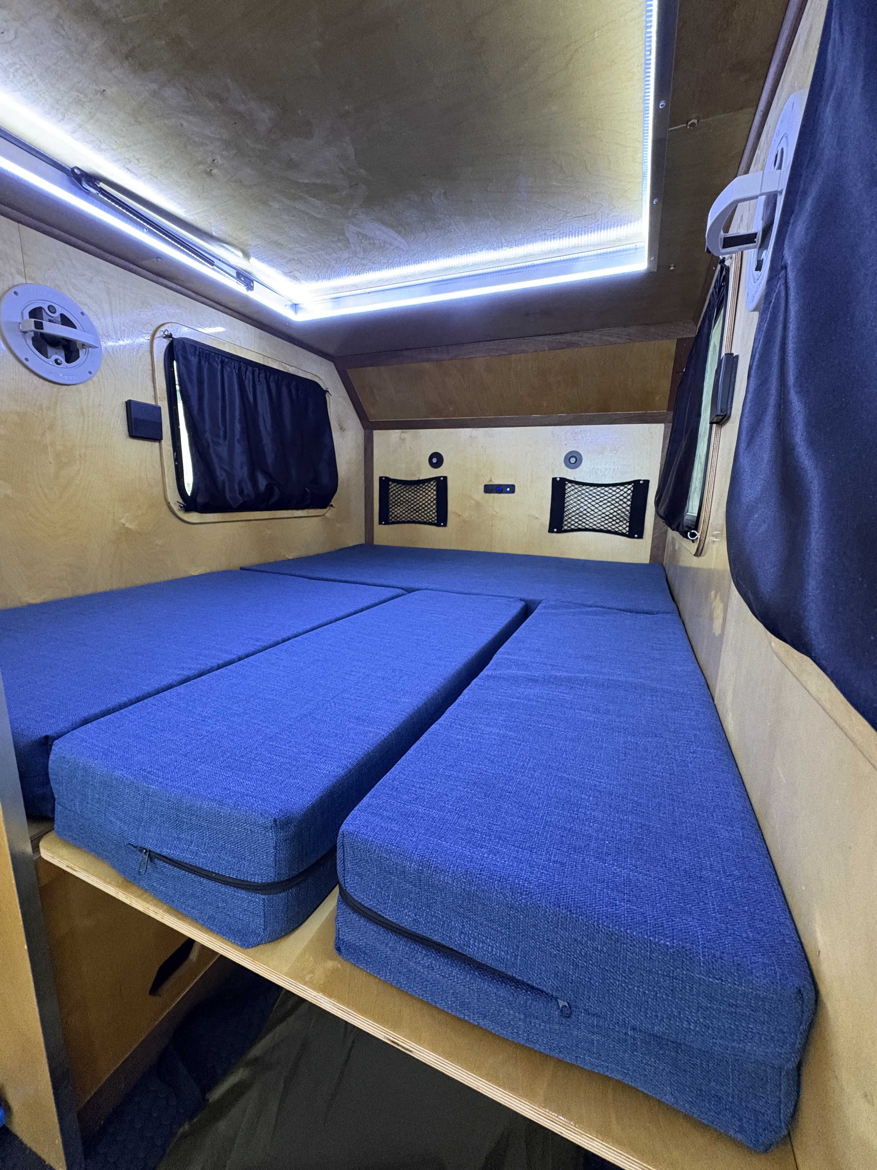 Interior of an RV rental: blue modular bed setup, bright LED ceiling lights, and wooden paneling.. Venture XL Off road 2025