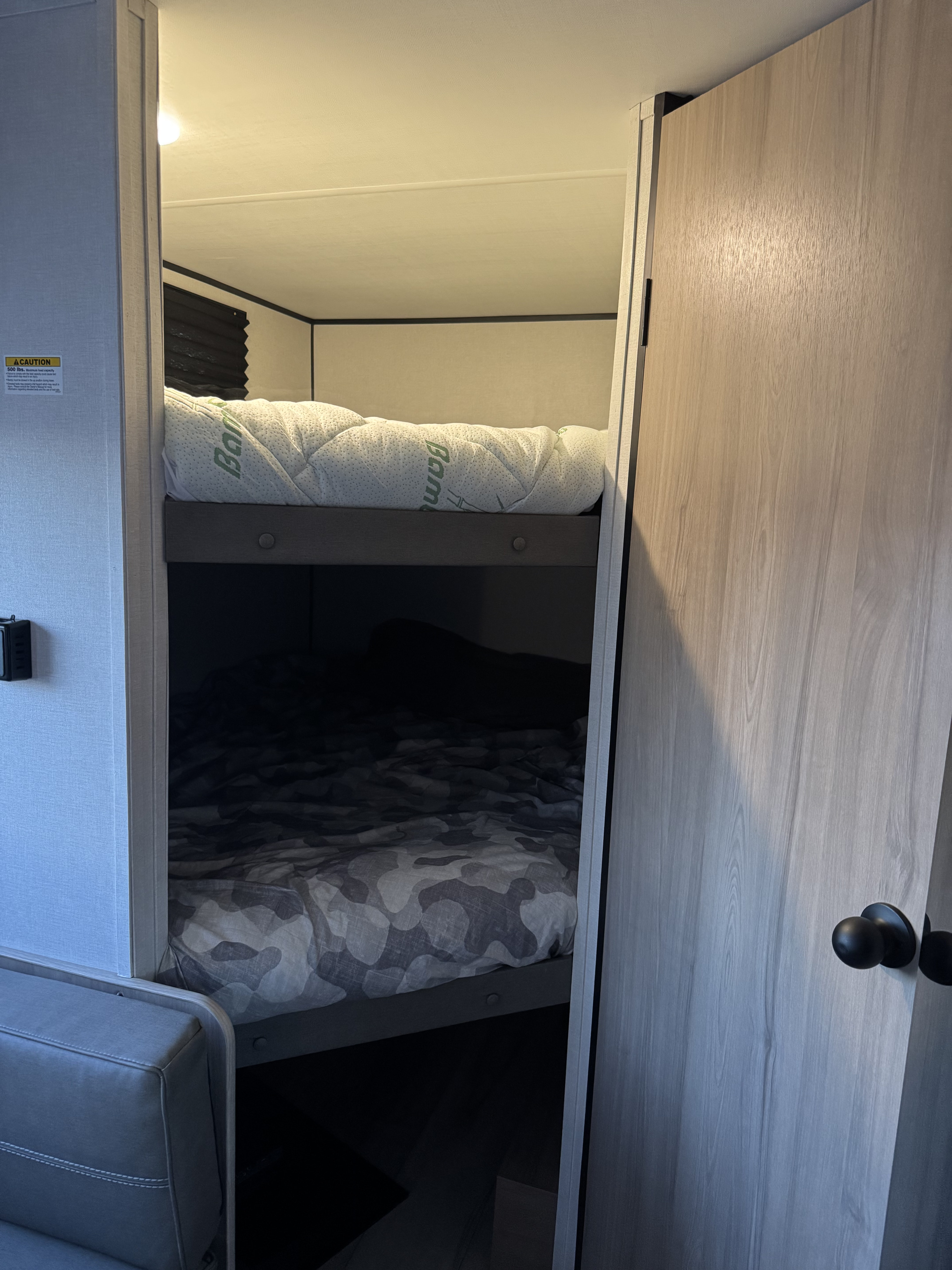 RV rental bunk beds: View of a compact sleeping area with a quilted top mattress and a camo-patterned lower bed.. Colman 23B 2025