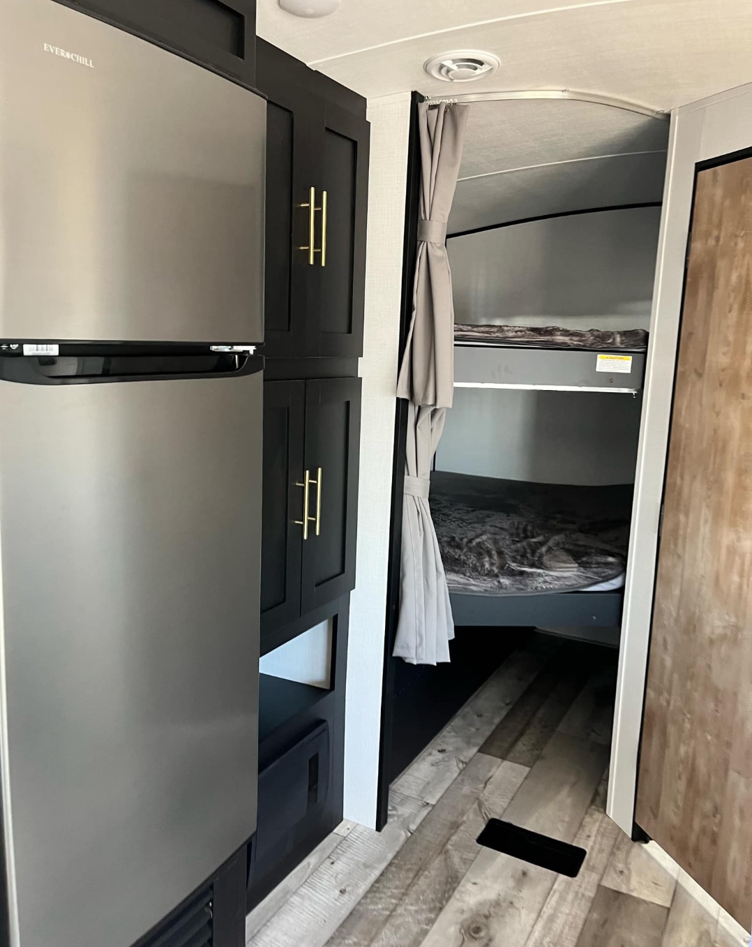Compact RV rental interior featuring a fridge, dark cabinets, and cozy bunk beds behind privacy curtains.. Keystone RV Springdale 2023