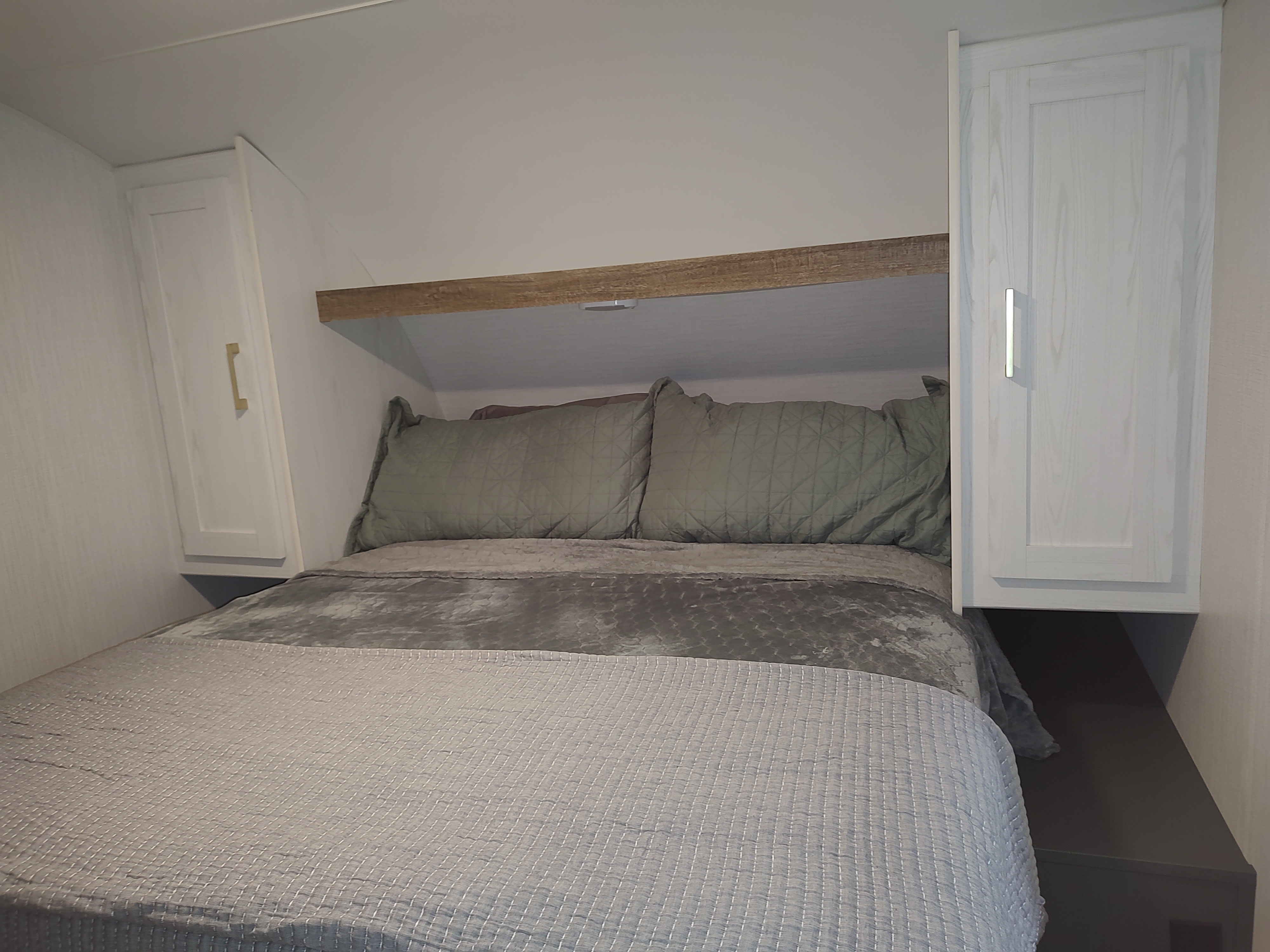 Cozy RV rental bedroom featuring a comfortable bed, overhead shelf, and stylish wall-mounted cabinets for efficient space.. Heartland RVs Eddie Bauer 261BHC 2024