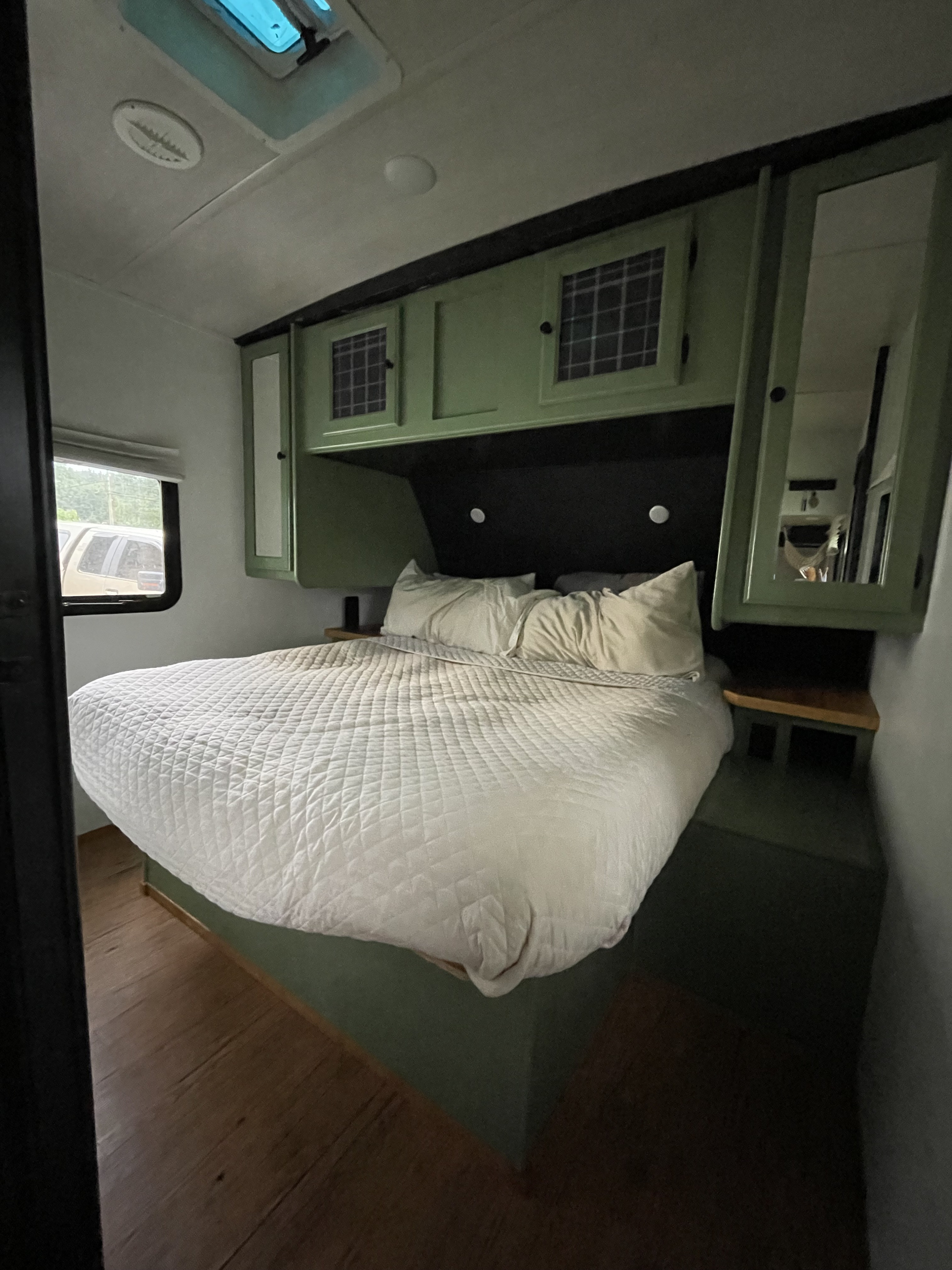 Cozy RV rental bedroom featuring a comfortable quilted bed, sage green cabinets, and ceiling skylight.. Heartland RVs Wilderness 2018