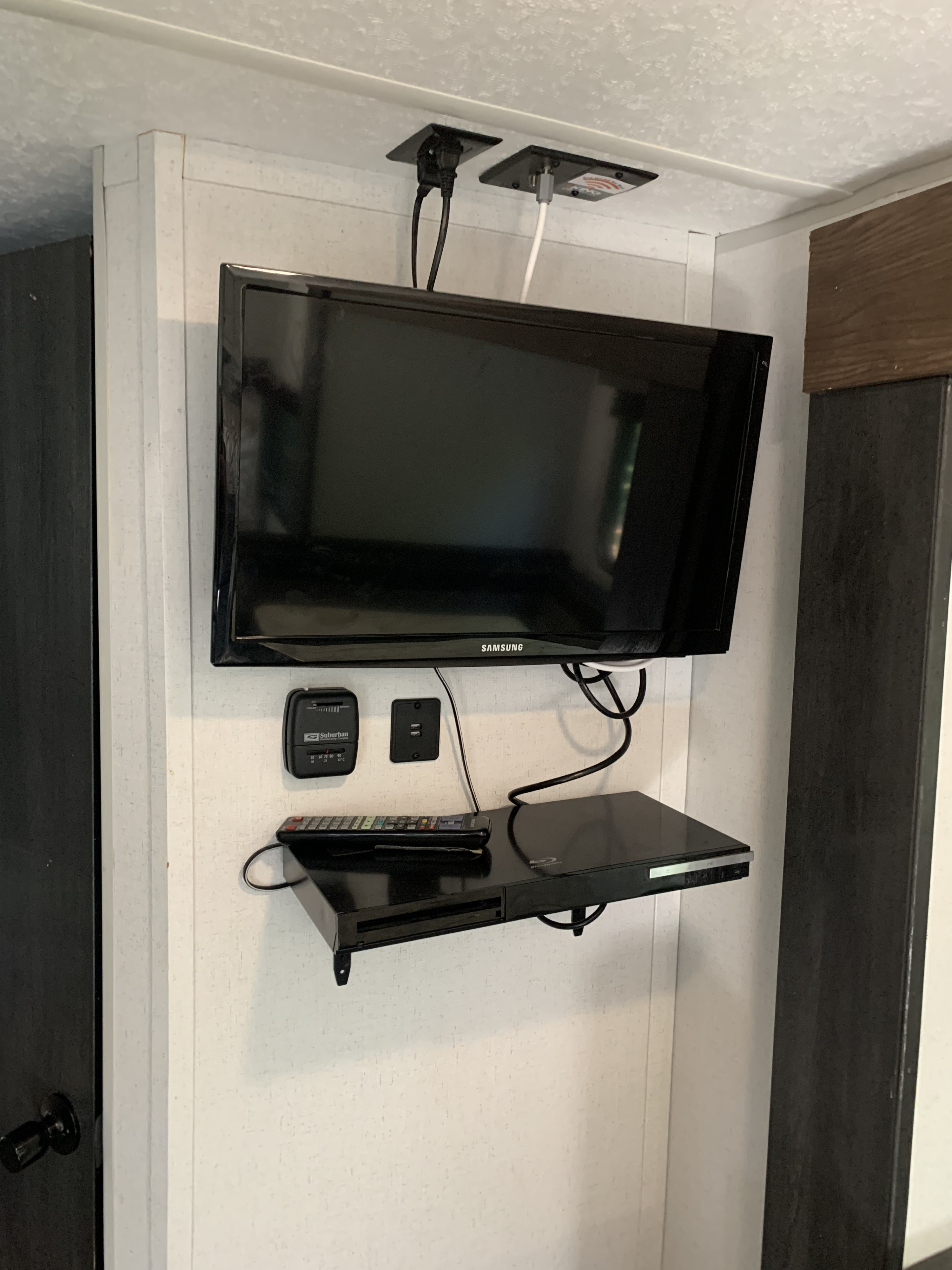 A wall-mounted TV, Blu-ray player, and thermostat create an entertainment hub inside this RV rental unit.. Forest River Salem FSX 2021