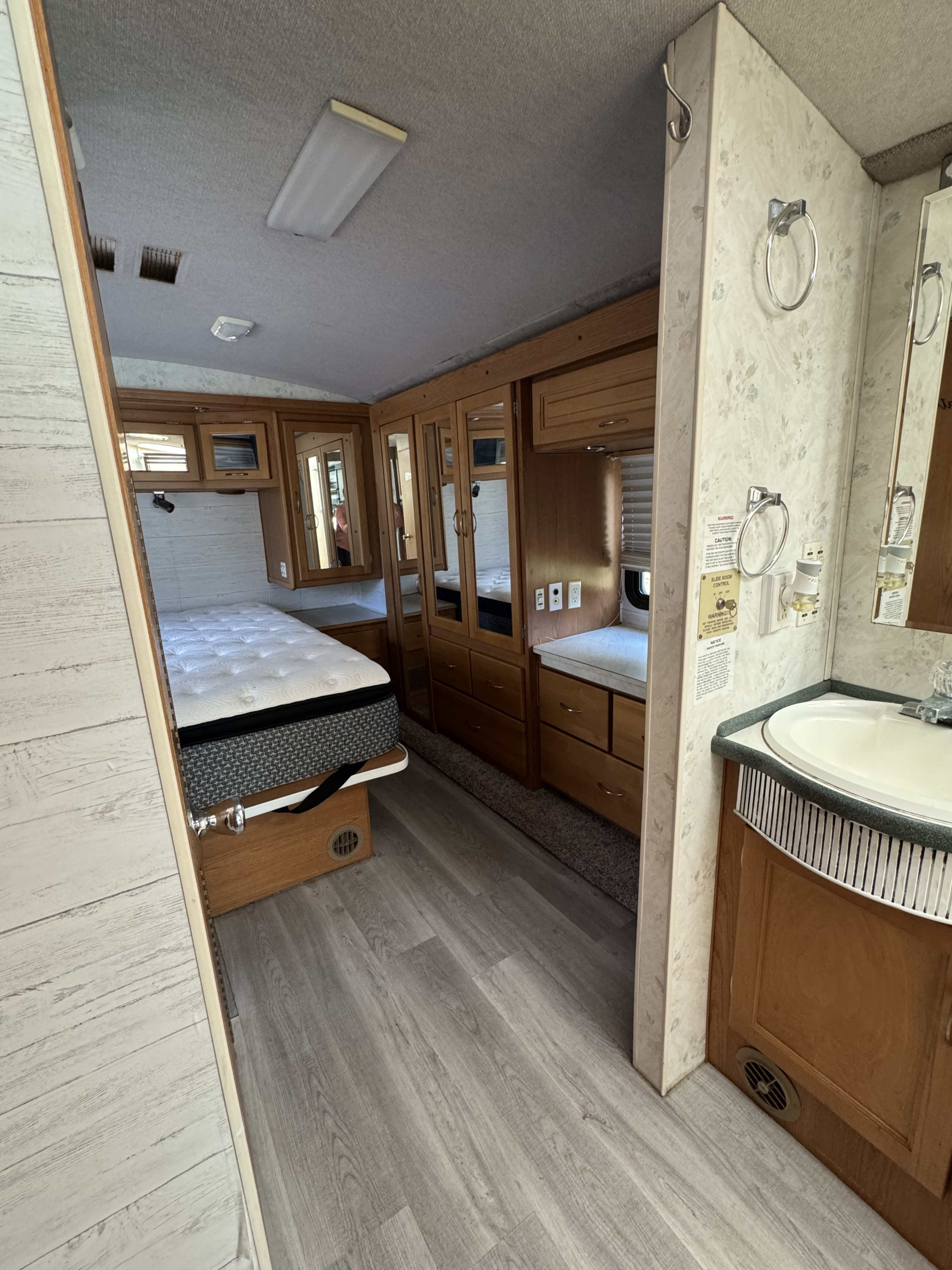 Inside an RV rental showing a bedroom with mattress, wood cabinets, mirrored closets, and a bathroom vanity with sink.. Fleetwood Southwind 36T 2000