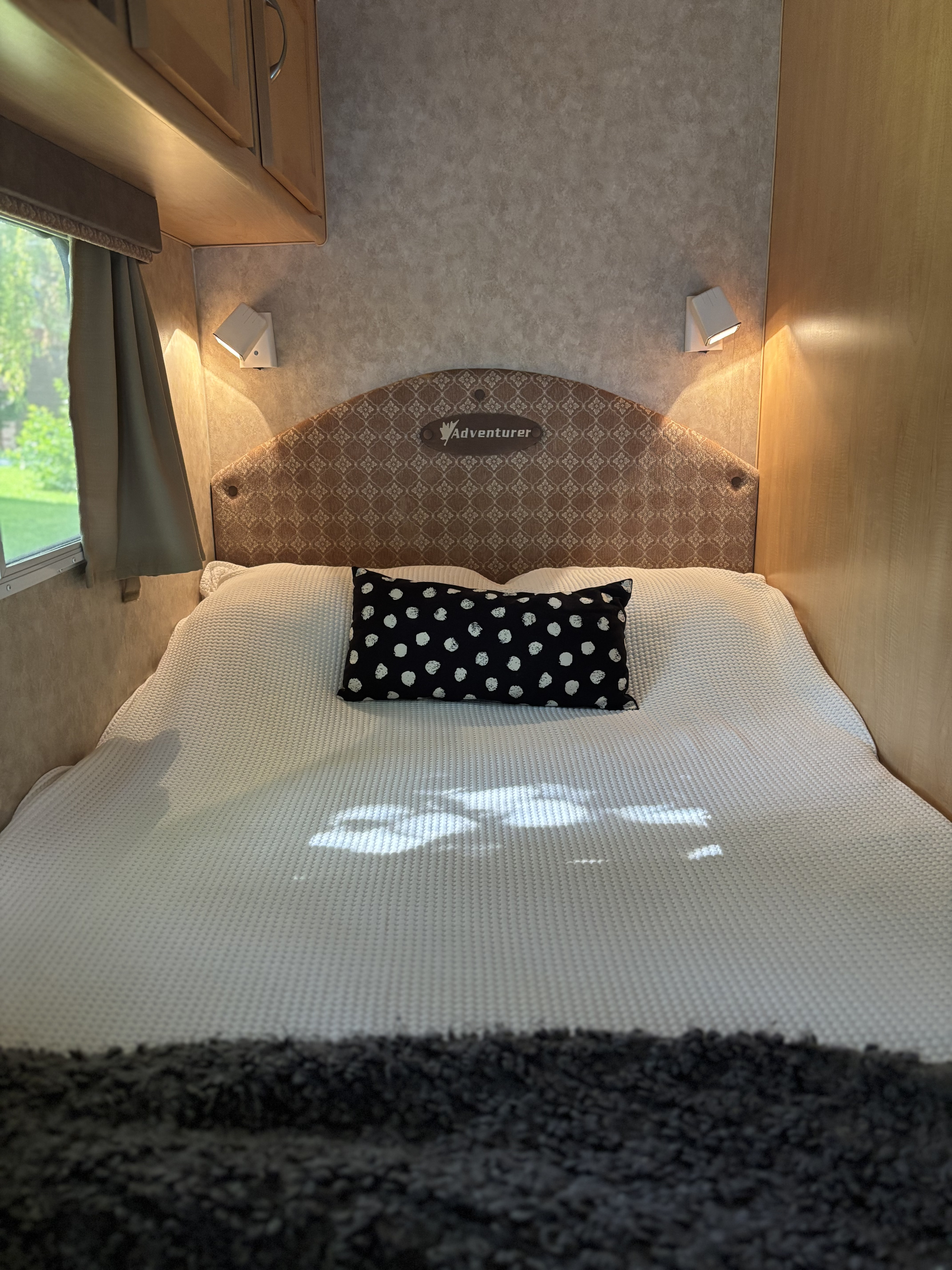 Inside an RV rental: a cozy bedroom featuring a white textured blanket, black polka dot pillow, and warm reading lights.. Adventurer Adventurer Motorhome 2008