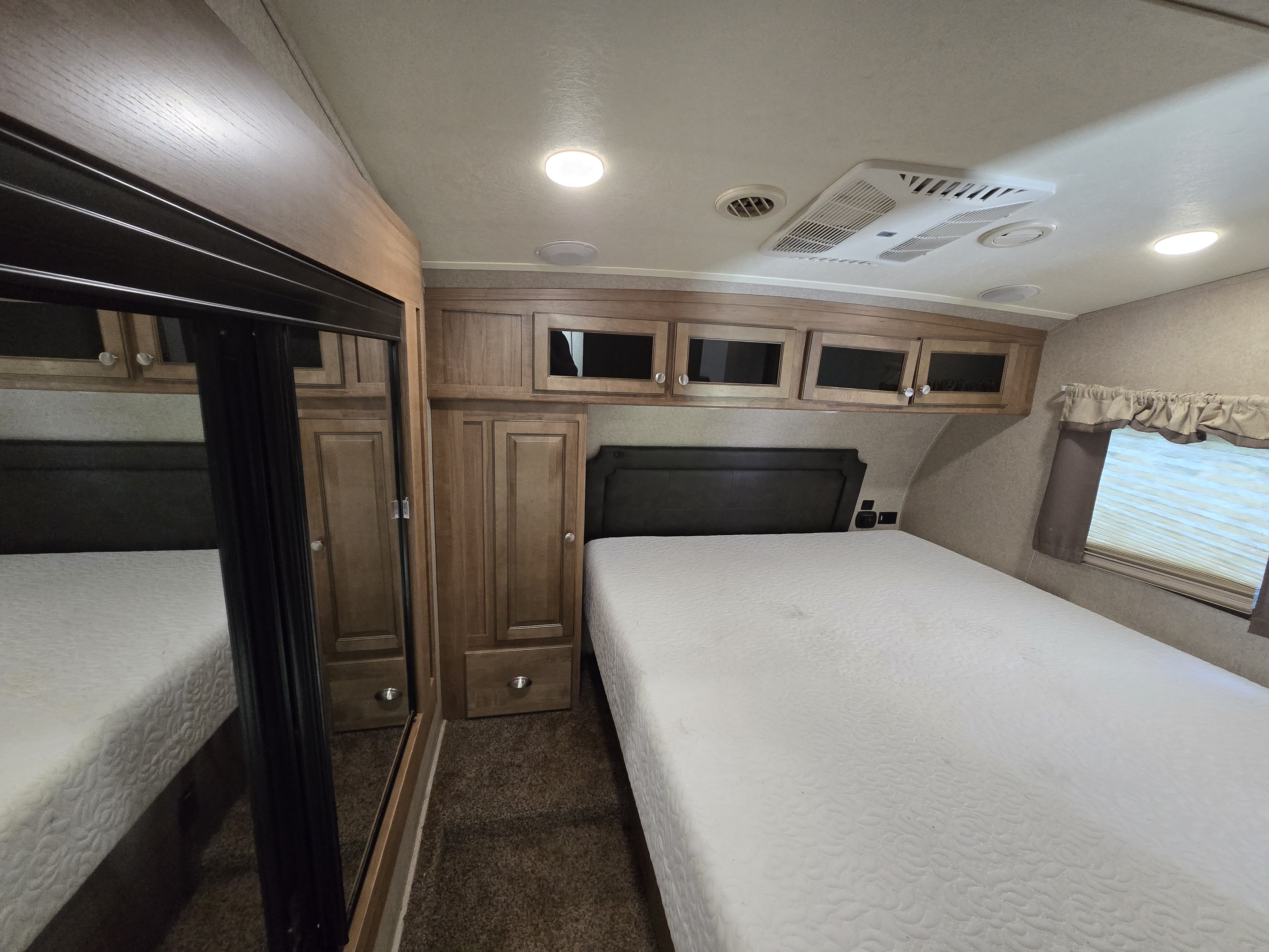 Cozy RV rental bedroom features a comfy queen bed, mirrored wardrobe, and overhead storage cabinets.. Forest River Rockwood Signature Ultra Lite 2018
