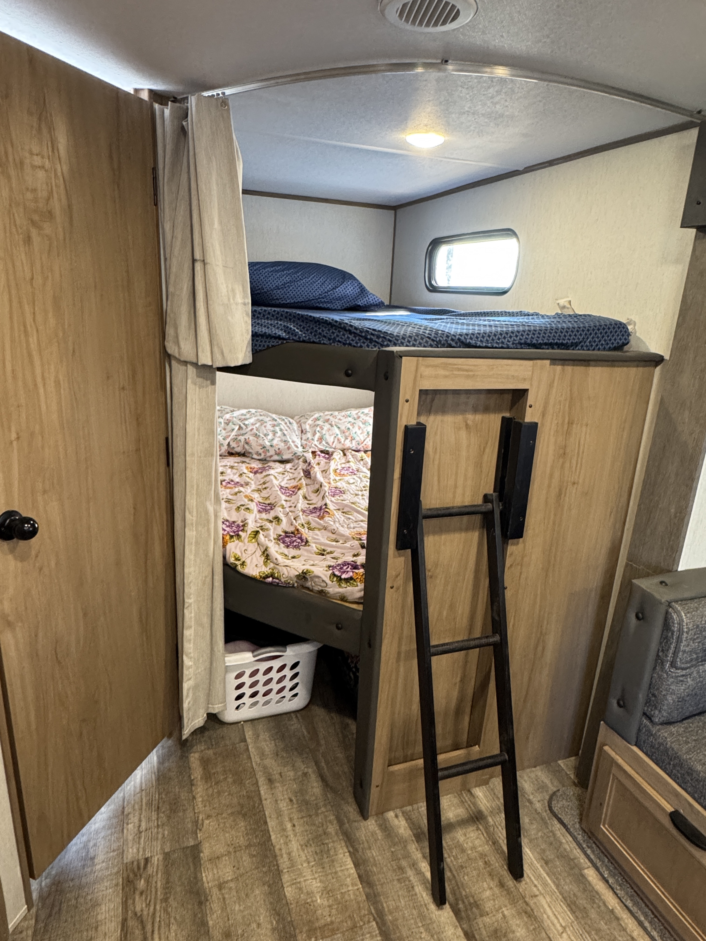 RV rental interior features bunk beds with blue and floral bedding, a ladder, window, and wood-look floor.. Forest River Cherokee Alpha Wolf 2024