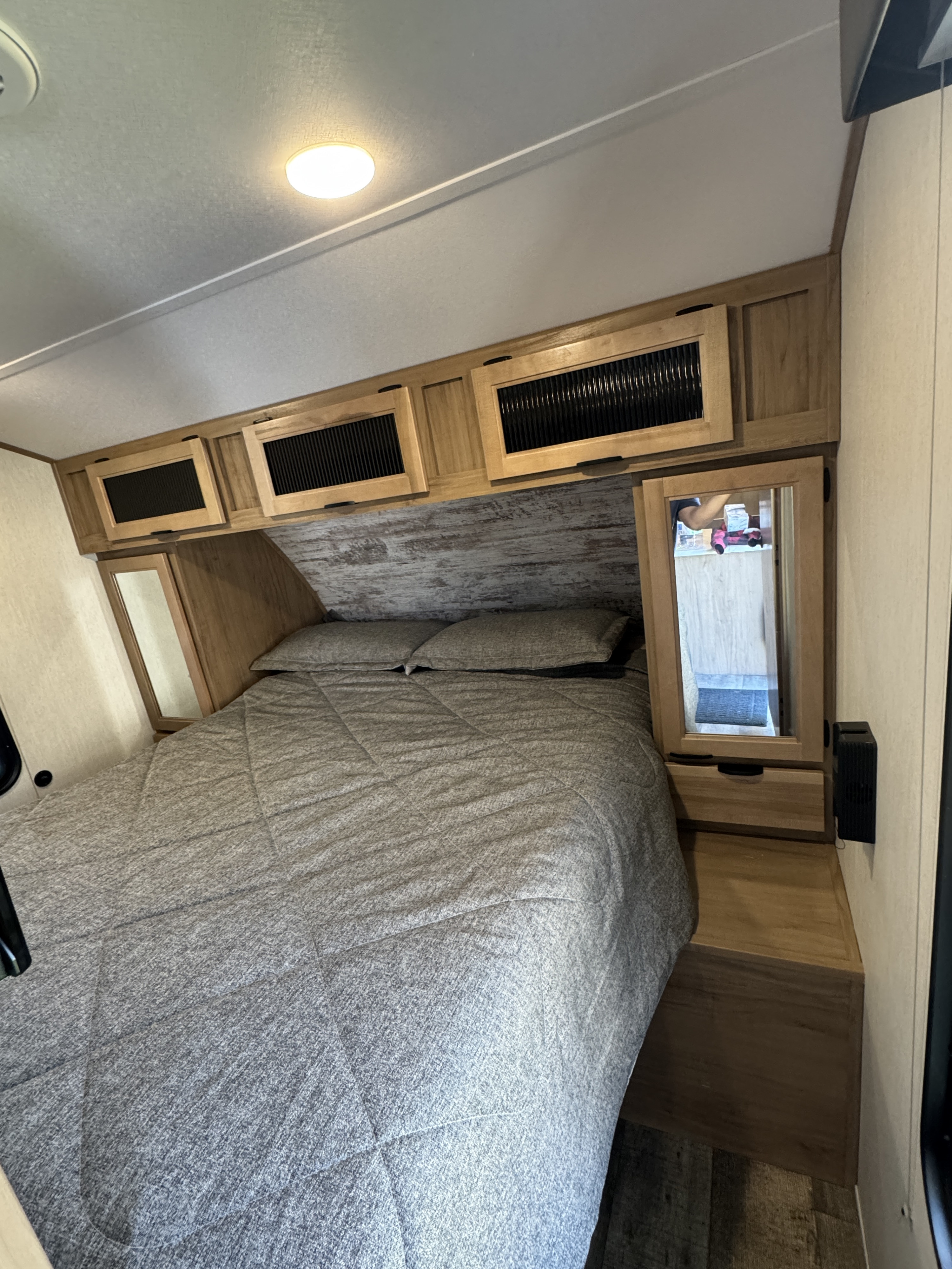 Inside an RV rental, a cozy bedroom features a neatly made bed with grey bedding and overhead wooden cabinets.. Forest River Cherokee Alpha Wolf 2024