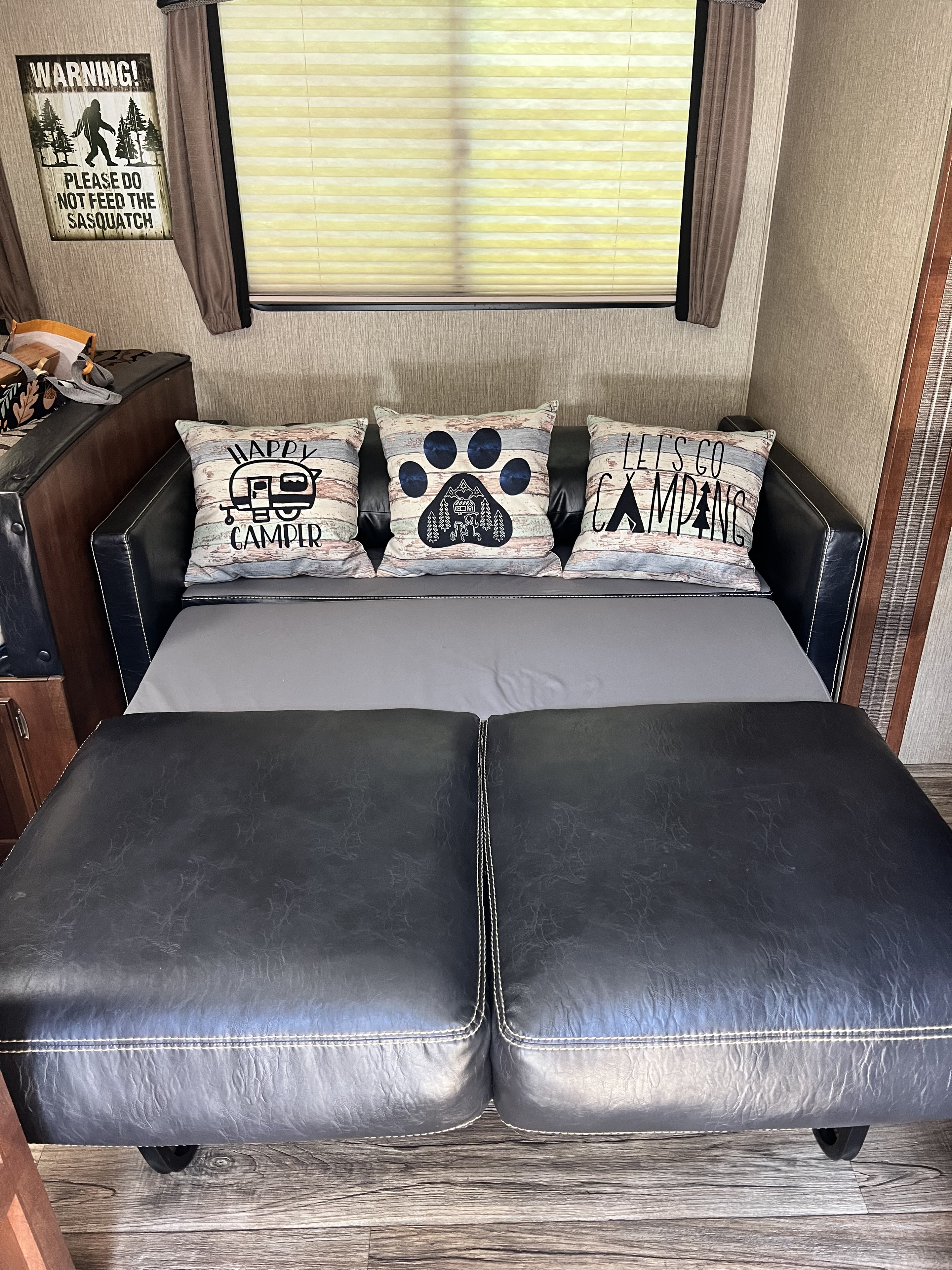 Cozy RV rental interior featuring a sofa bed with camping-themed pillows and a fun "Sasquatch" warning sign.. Keystone RV Passport Grand Touring 2017