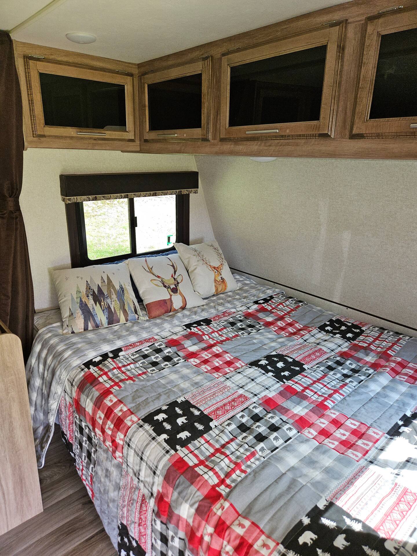 Cozy RV rental bedroom featuring a plaid quilt, deer-themed pillows, and overhead wooden cabinets.. Jayco Jay Feather 2018