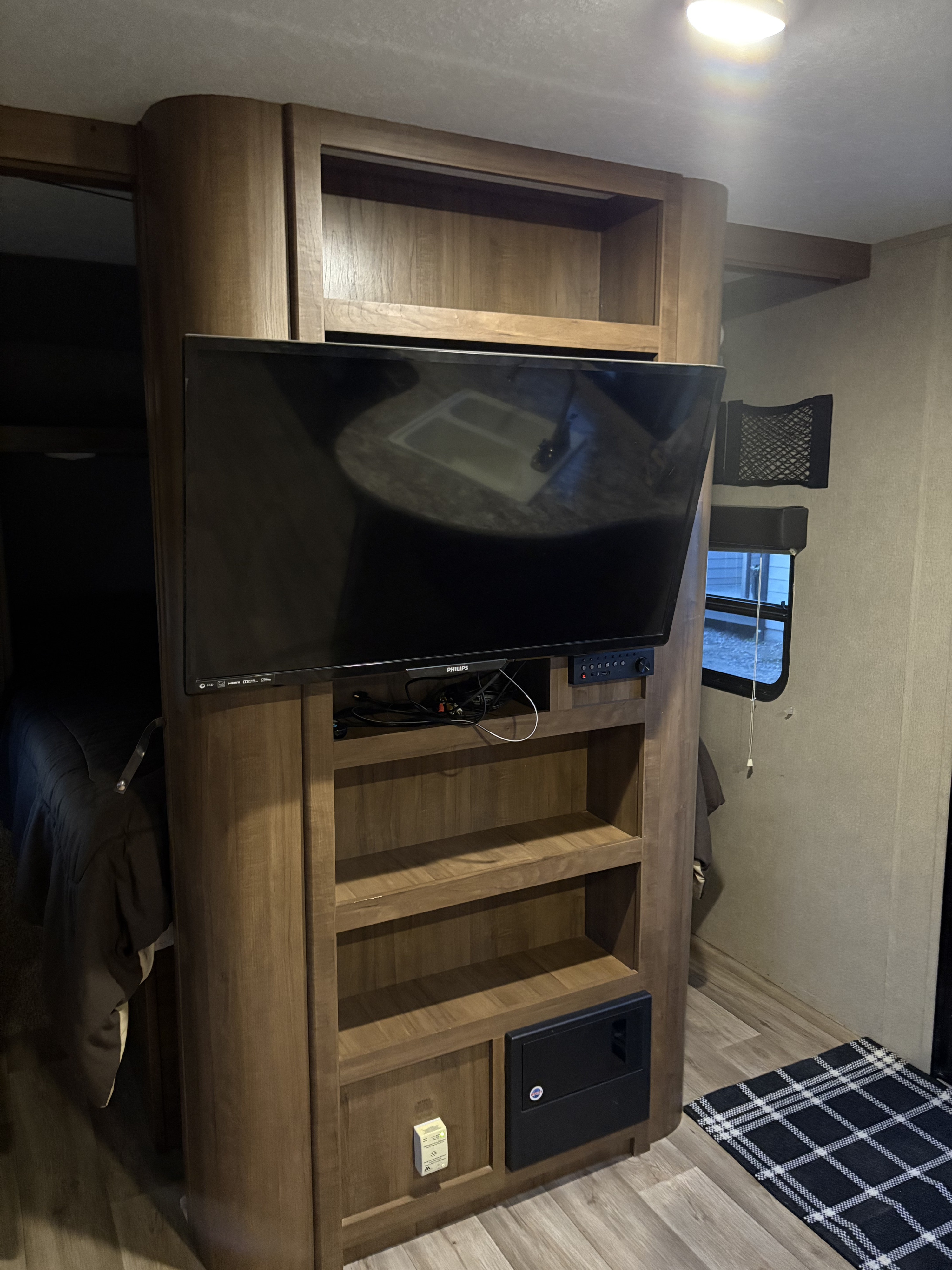 RV rental interior: Wooden entertainment center with a TV, stereo, shelves, and electrical panel. A bed and window are visible.. Aspen Trail Aspen Trail Trailer 2017